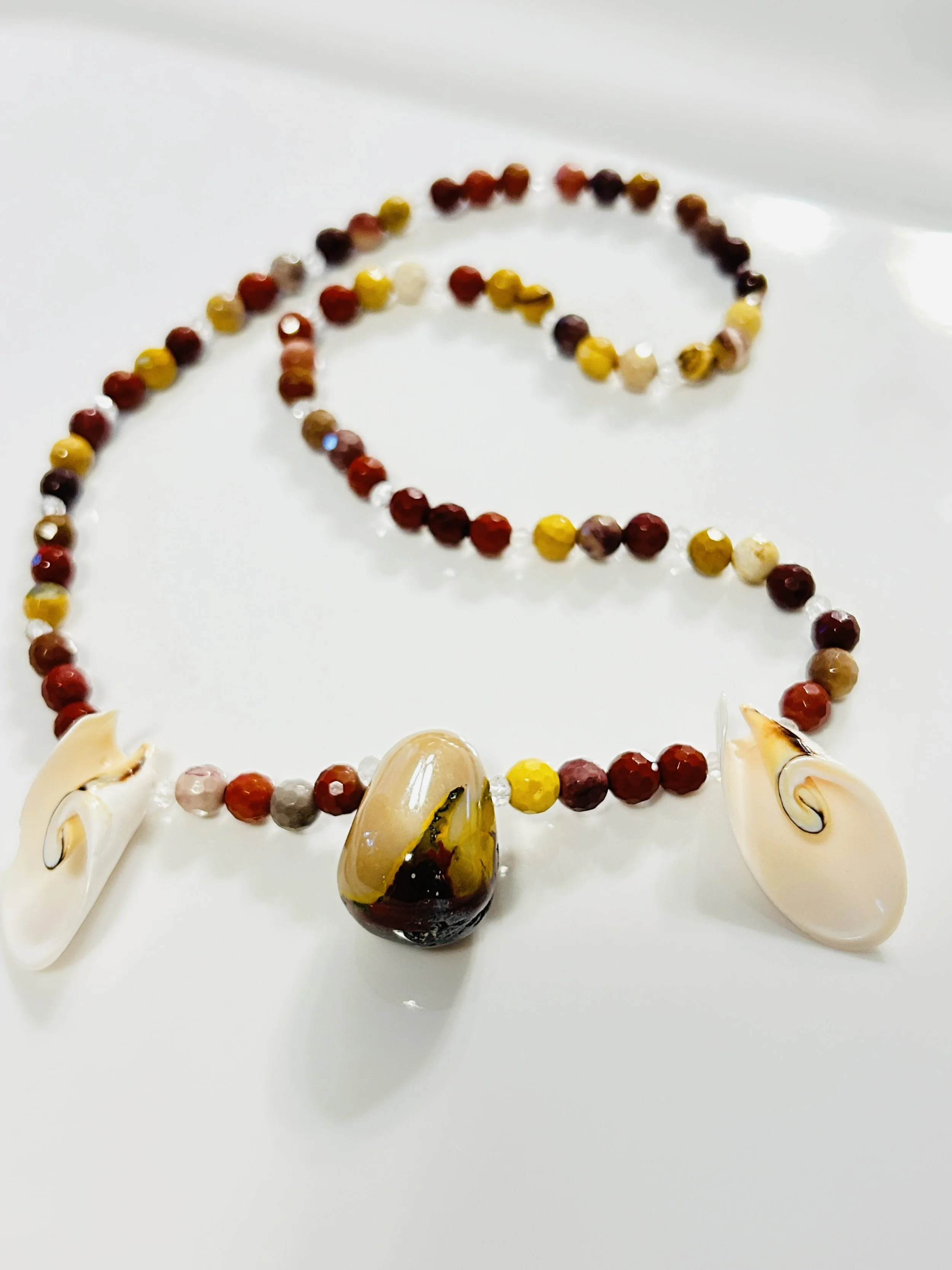 Beaded necklace with three large shell and stone pendants on a white background.