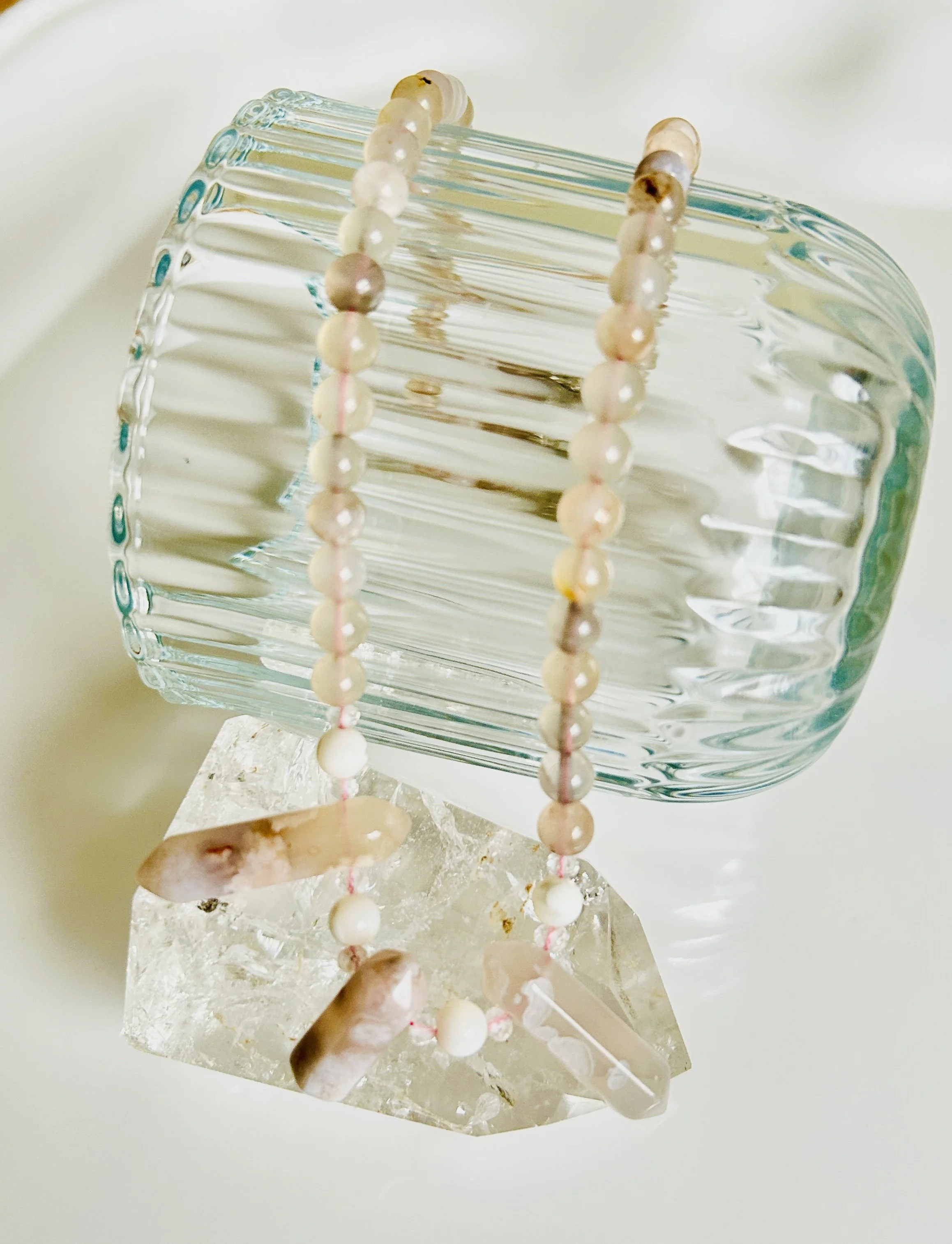A decorative crystal vase with a pearl necklace draped over it, placed on a clear crystal stand.