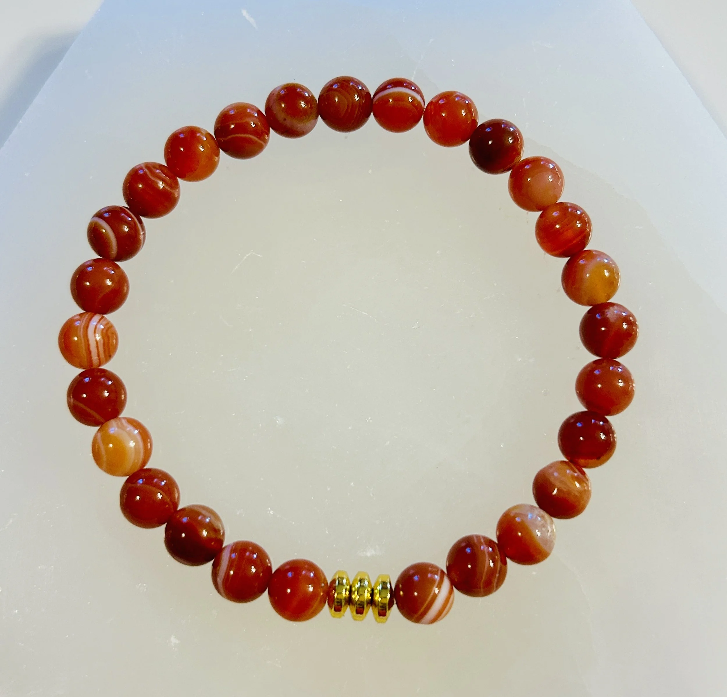 Red and orange striped beads forming a bracelet with three small gold beads in the center.