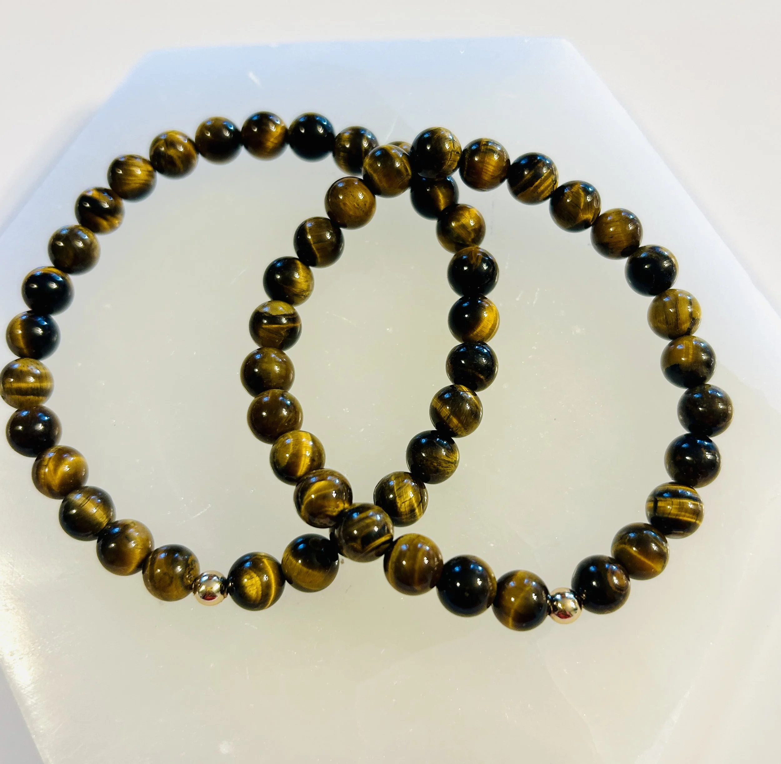 A tiger's eye gemstone bead bracelet with dark brown and golden striped beads, accented with small silver beads, displayed on a white surface.