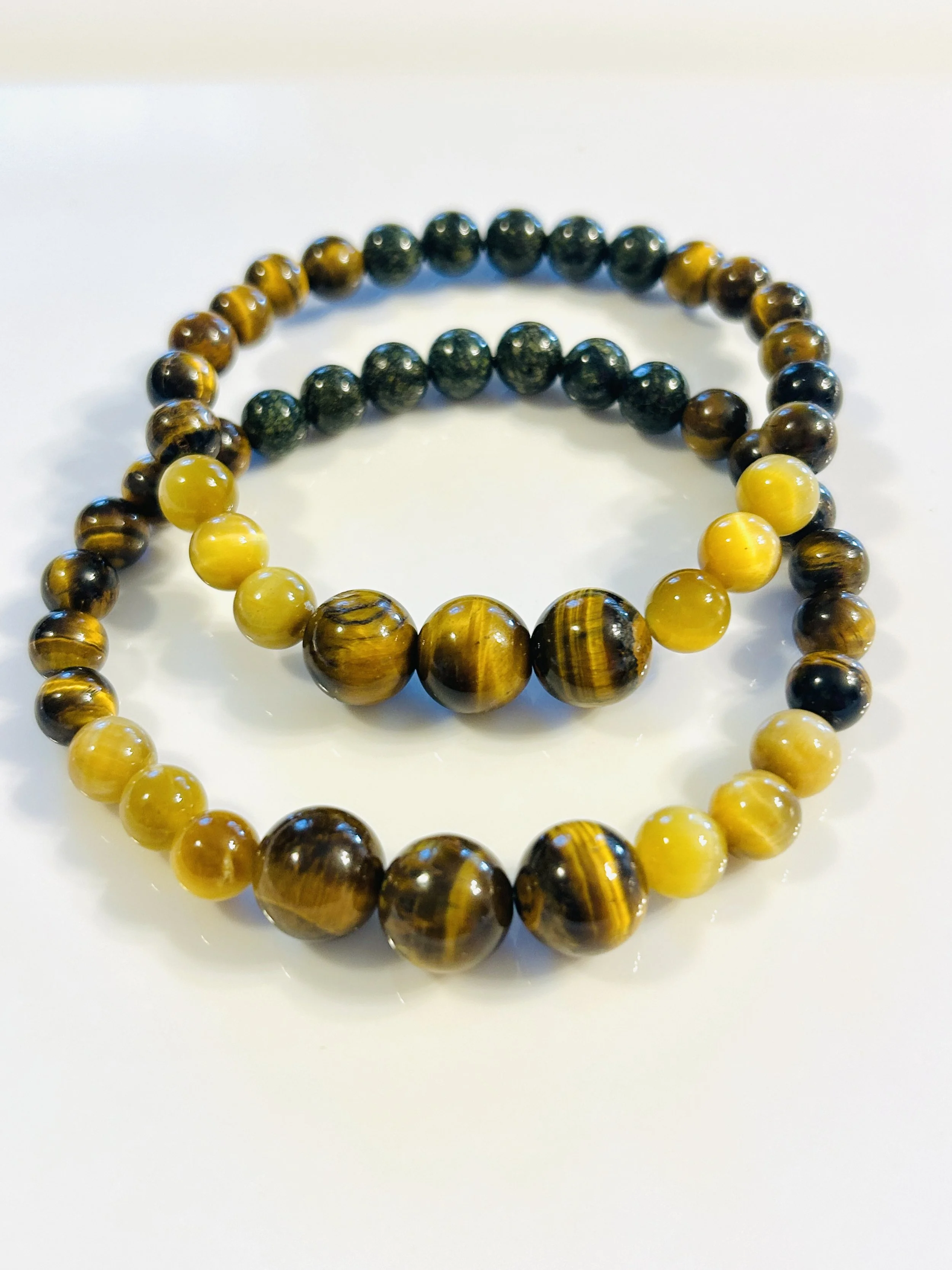 Two beaded bracelets, one with yellow and brown beads, the other with dark green beads, on a white surface.