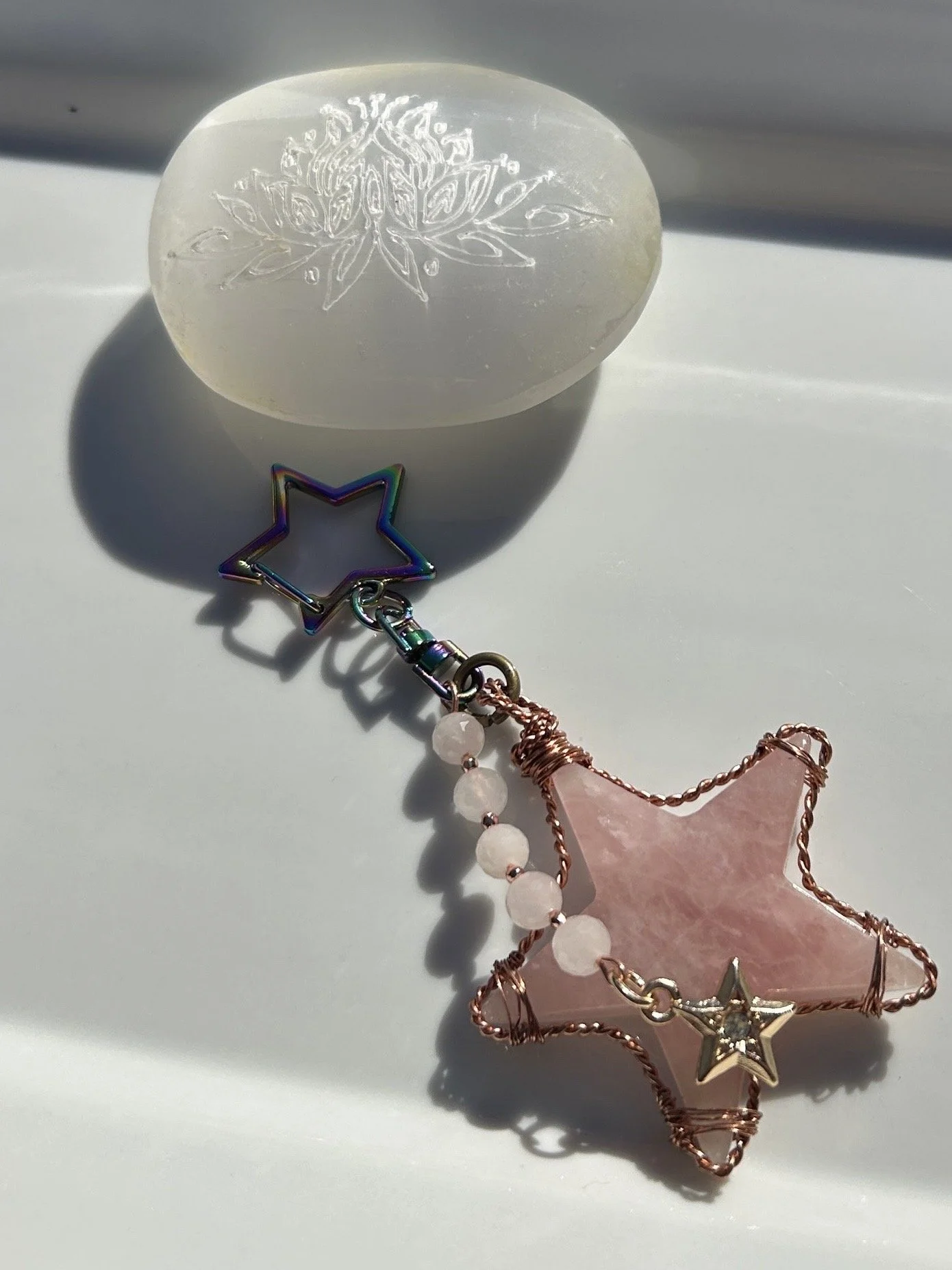 A white soap with an engraved snowflake design, a colorful star-shaped keychain, and a pink star-shaped jewelry piece with a small star charm and pink beads, all cast in soft sunlight on a white surface.