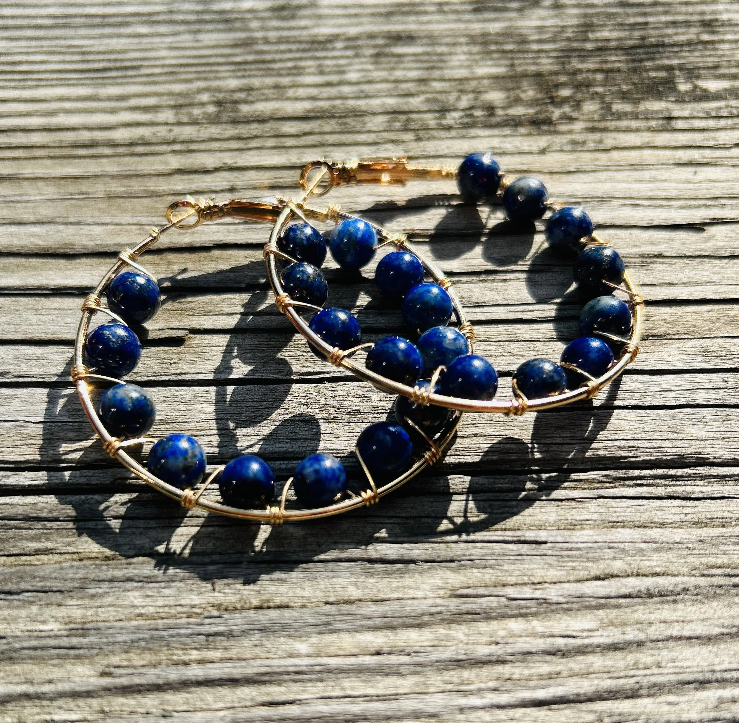 Blue beaded jewelry with gold wire on weathered wooden surface.