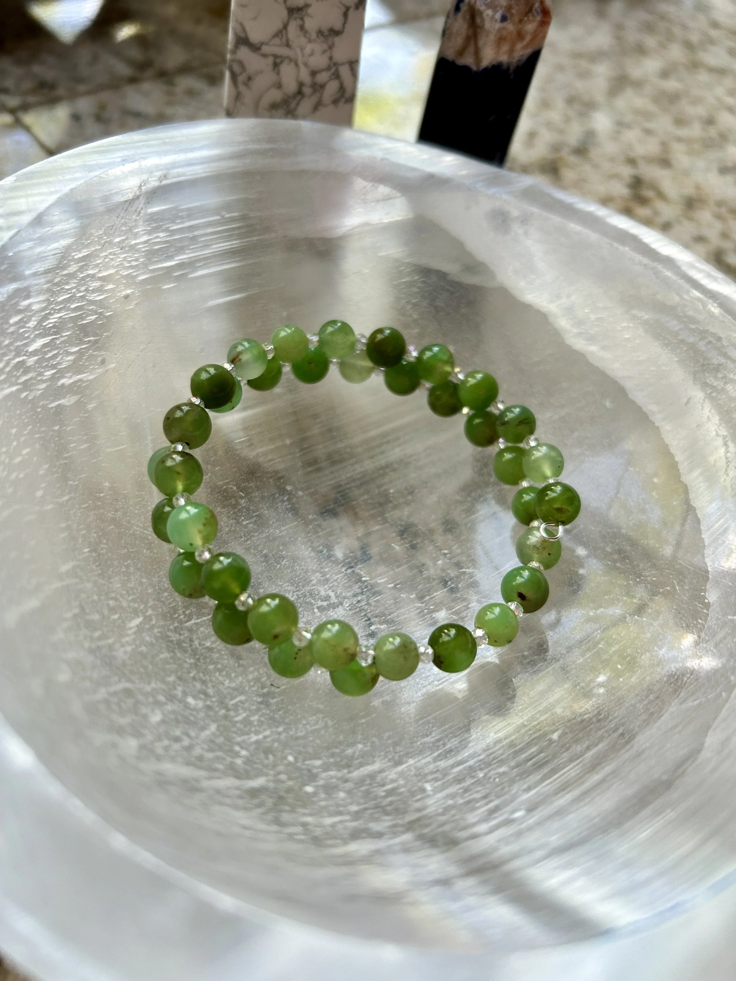 A green beaded bracelet resting on a clear glass dish.