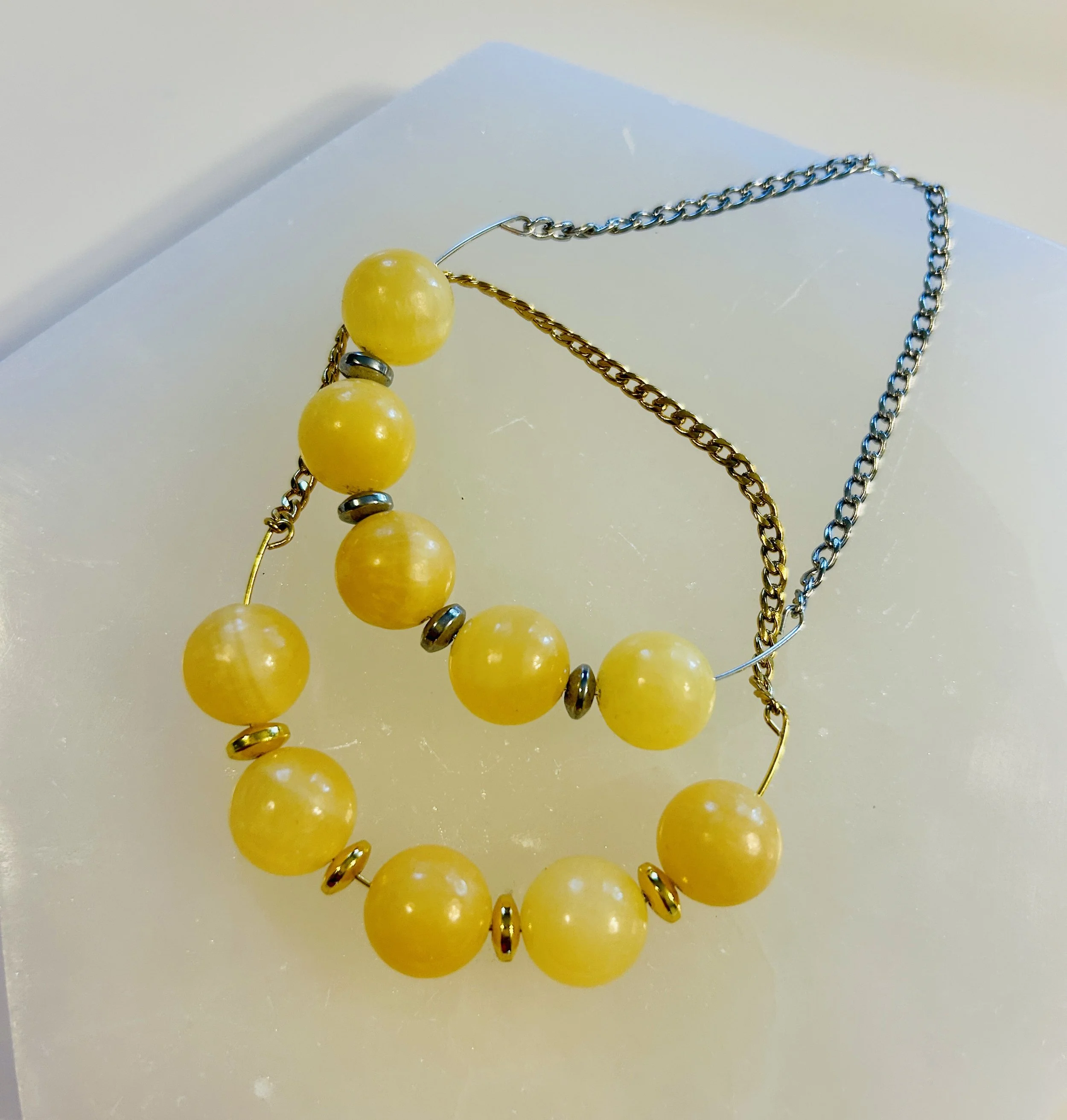 Yellow beaded necklace with alternating small metallic beads and a silver chain, placed on a white surface.