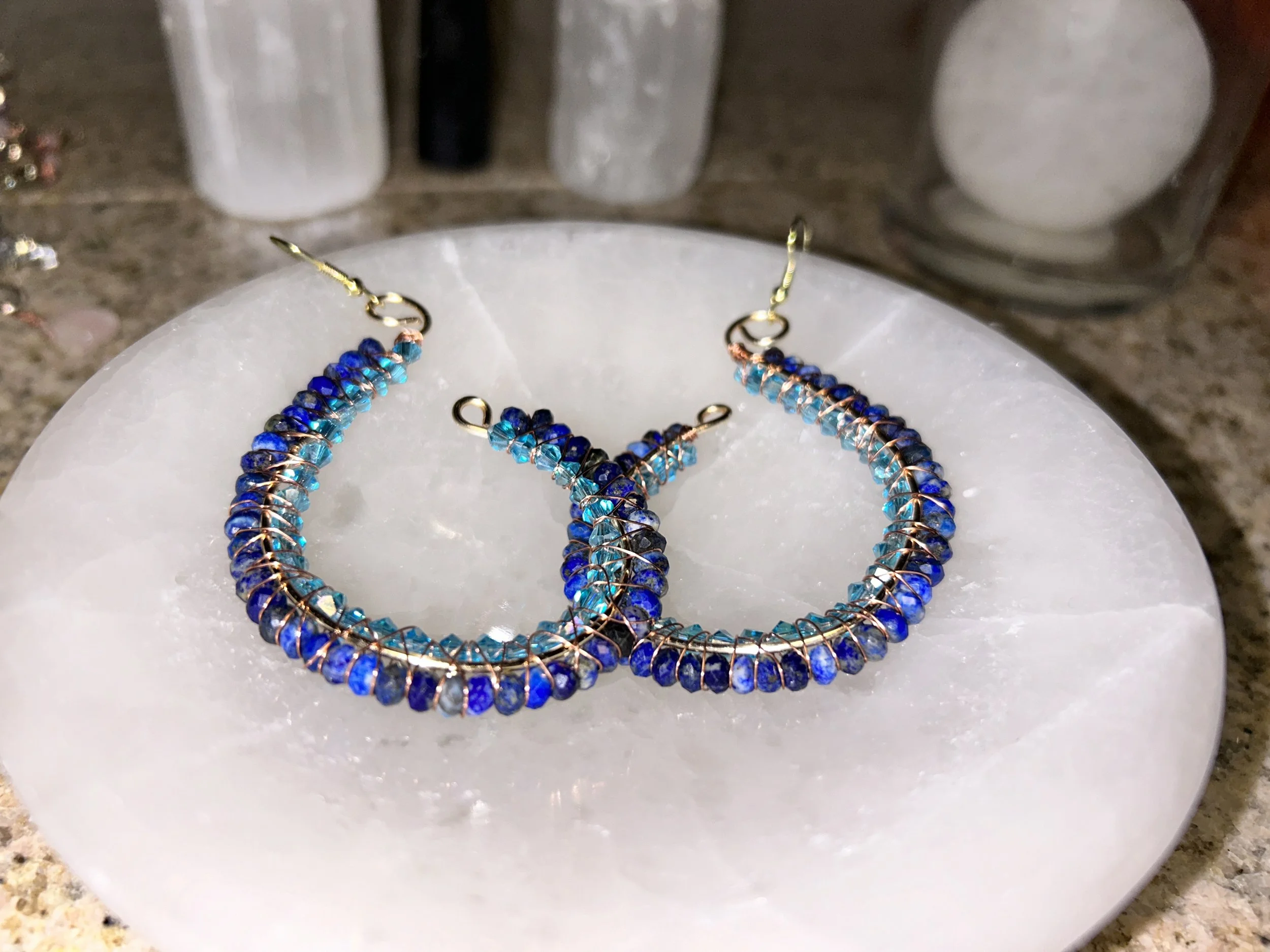 Pair of hoop earrings with blue and turquoise beads, displayed on a white marble dish.