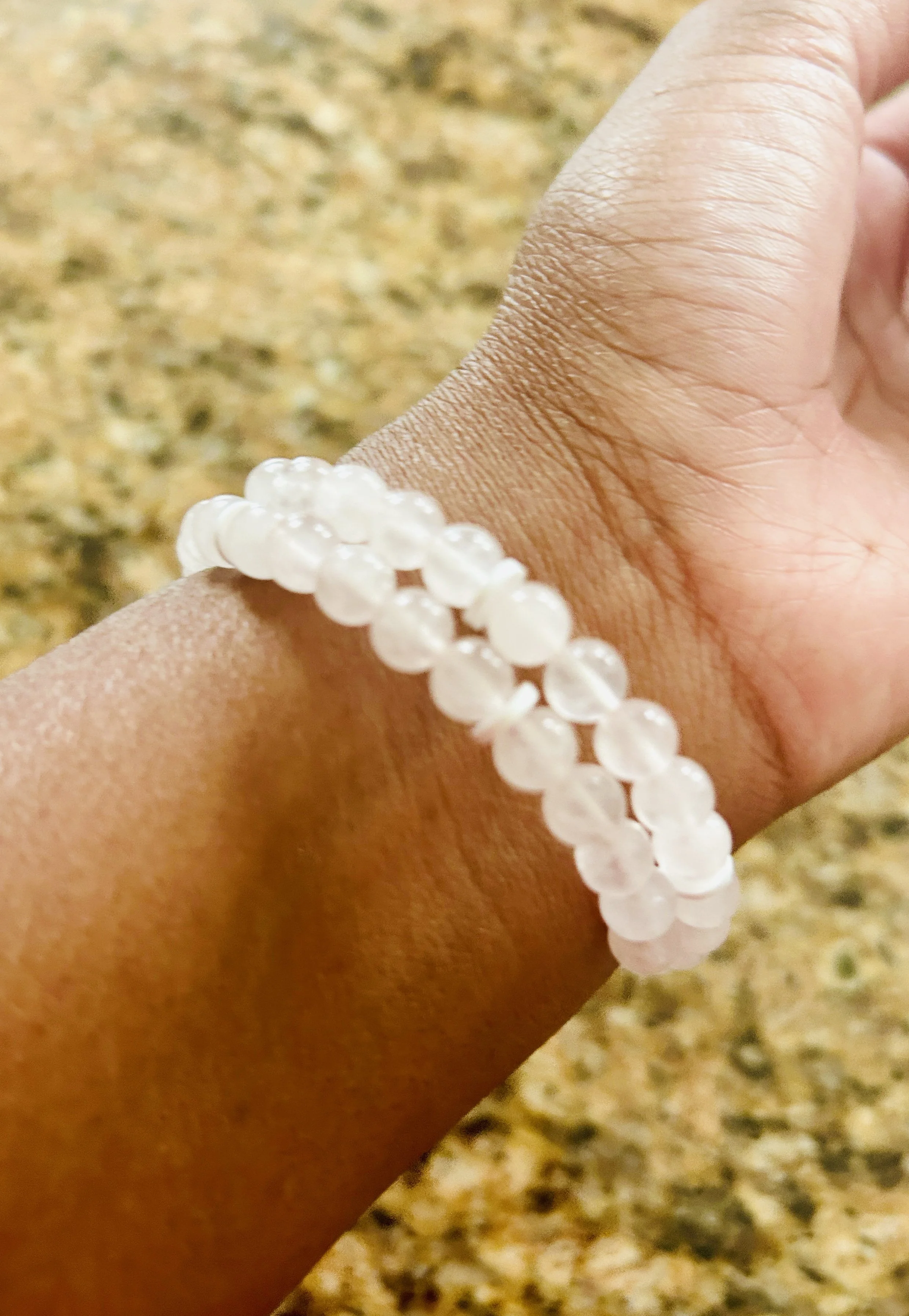 A hand wearing a white beaded bracelet against a granite countertop background.