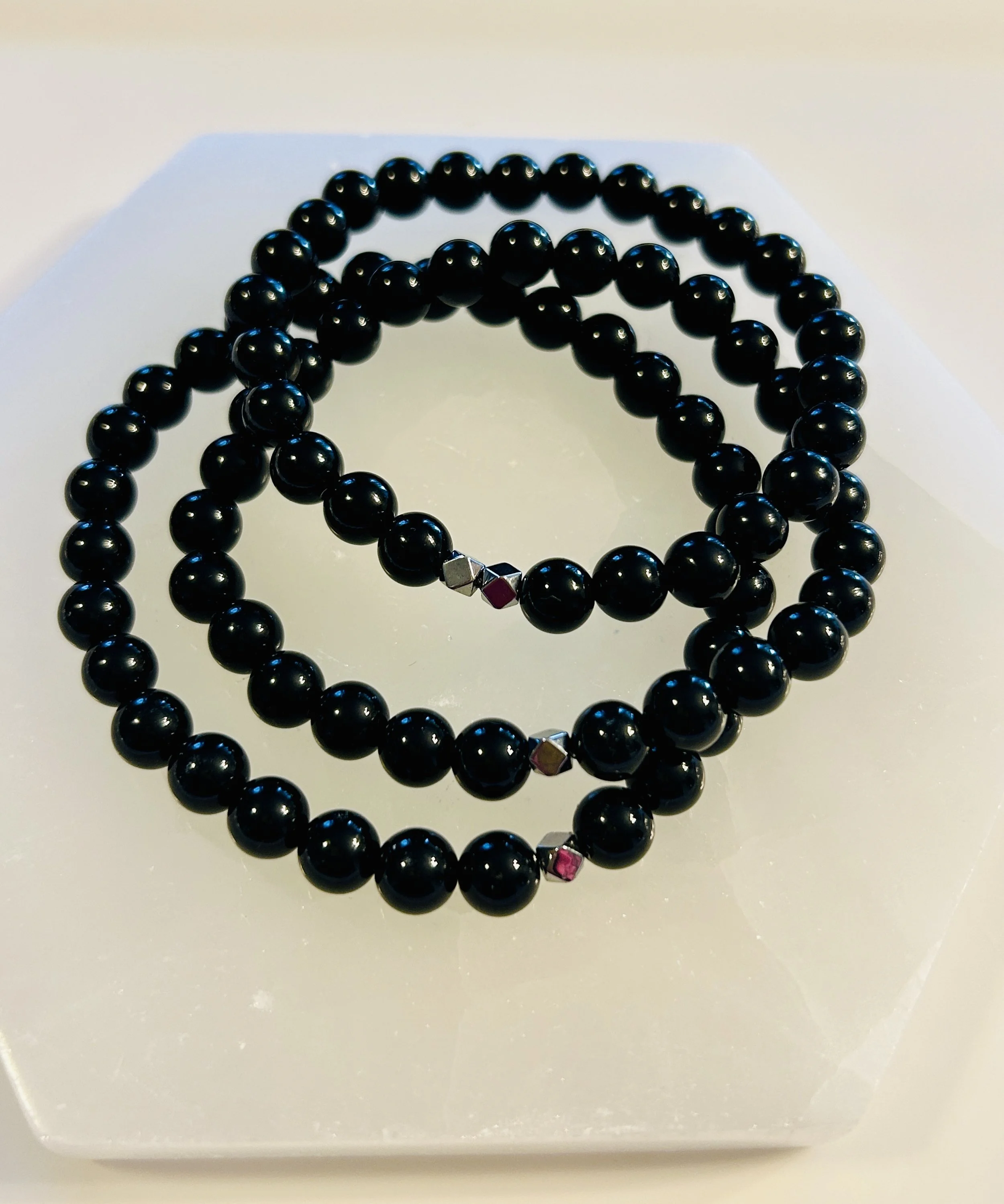 Black beaded necklace with small metallic beads, displayed on a white octagonal surface.