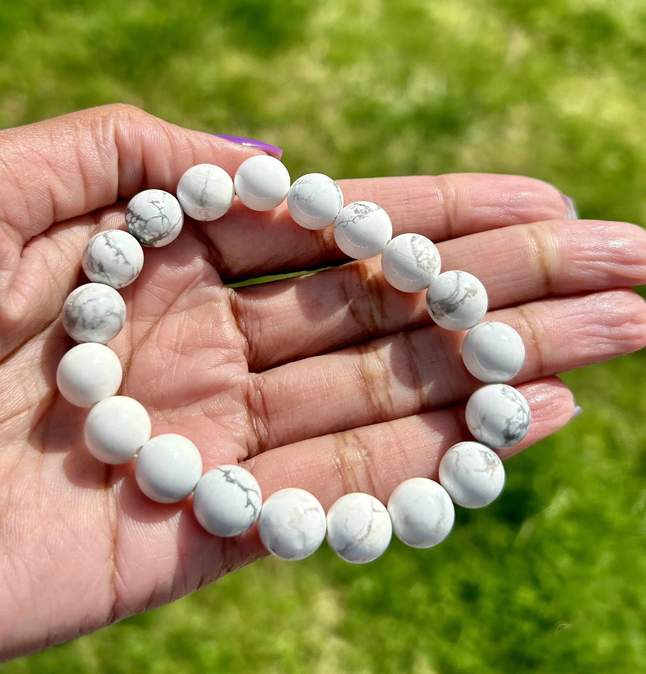 Hand holding a white marble beaded bracelet outdoors with grass in the background.