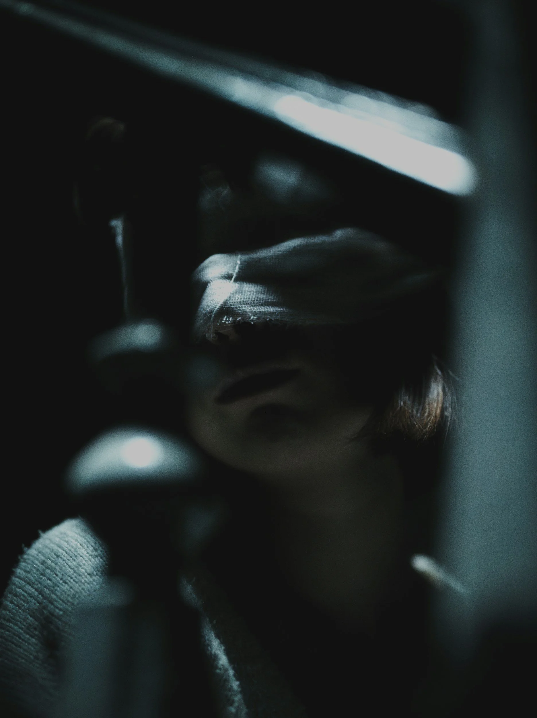 Dark, blurry close-up of a person wearing a light-colored, textured shirt, hidden face, with indistinct background and foreground elements.