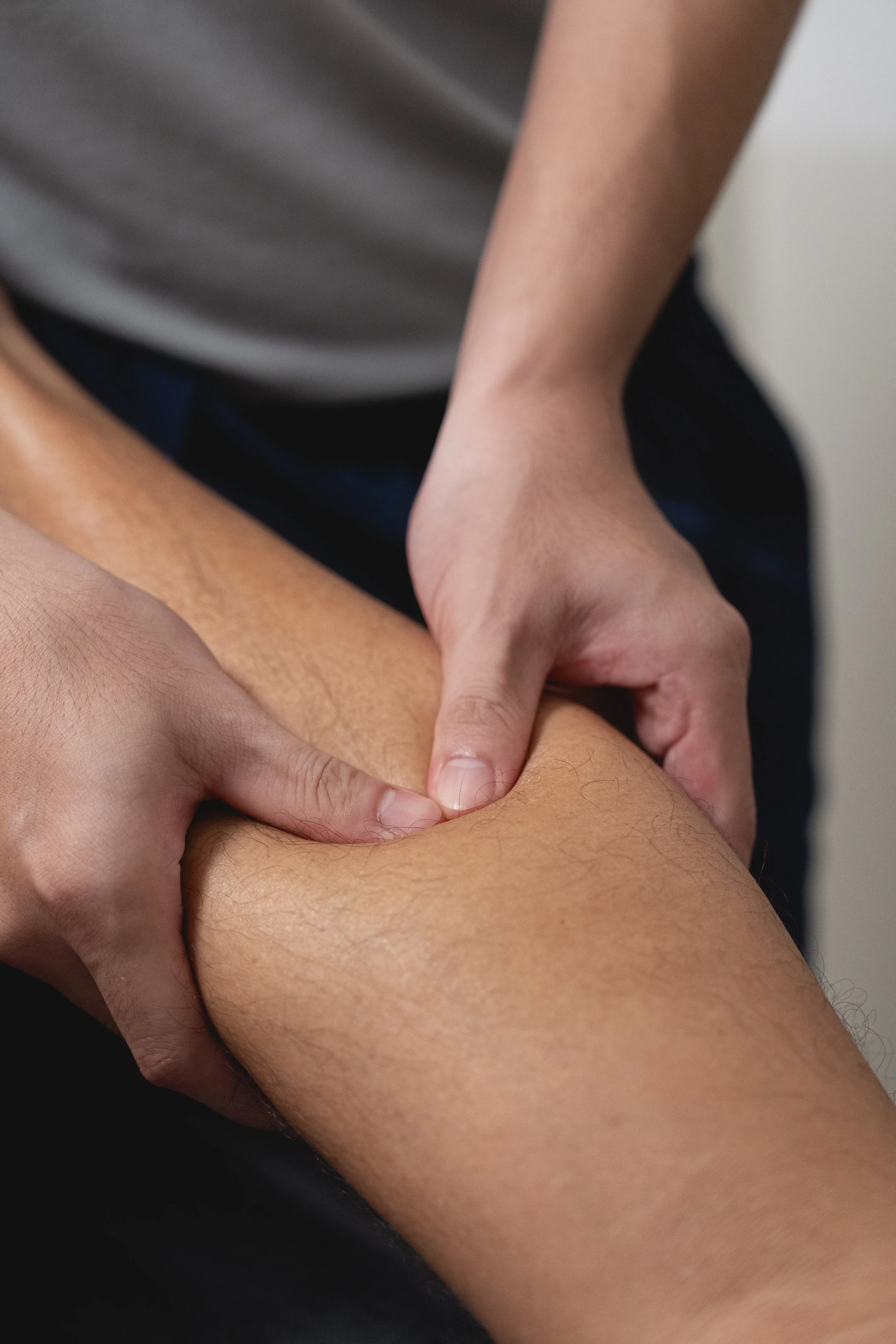 Close-up of a person receiving a massage, focusing on the hands applying pressure to the person's calf muscle.