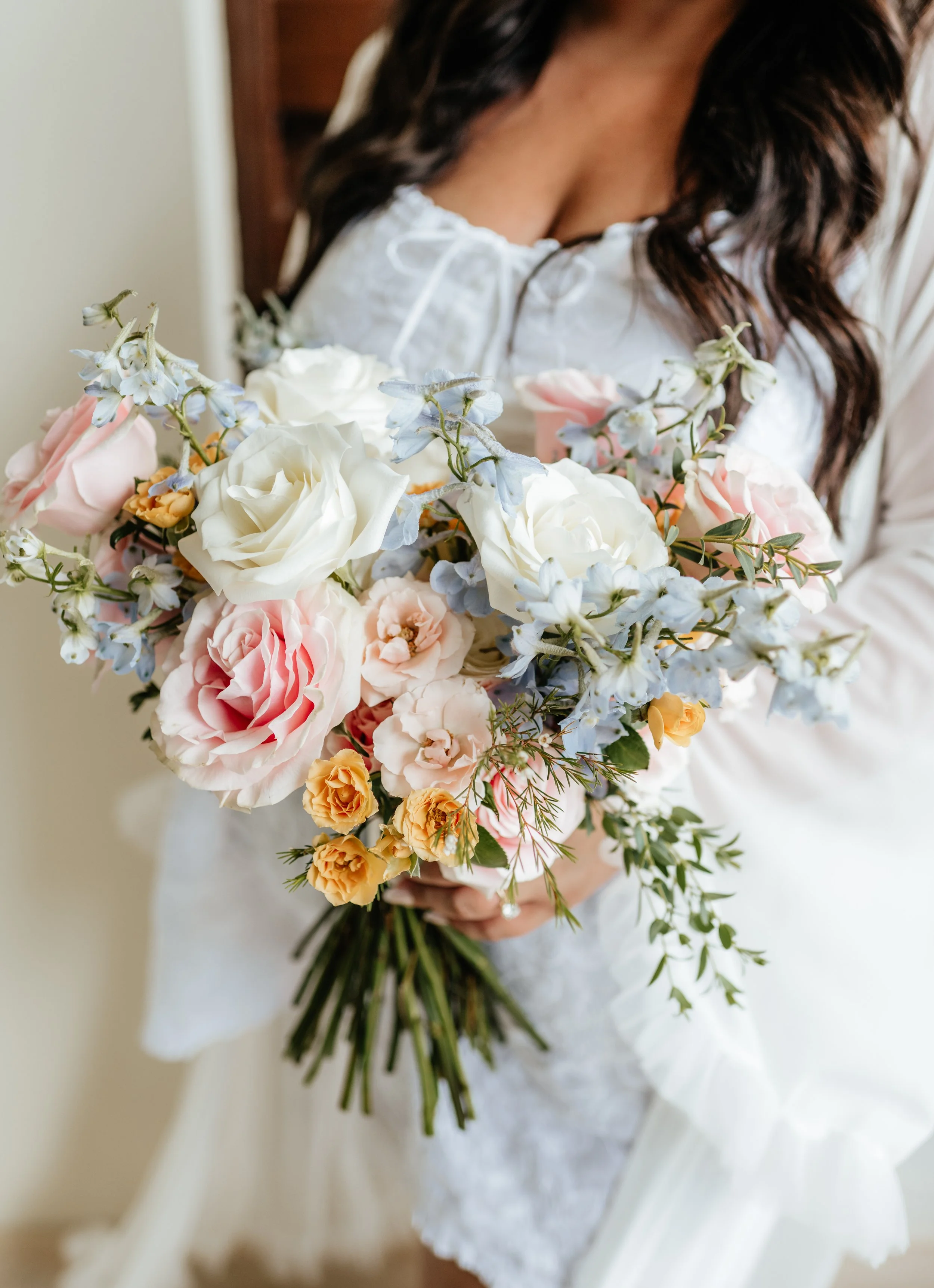 A woman in a white dress holding a large bouquet of flowers, including roses and other blooms in pastel shades.