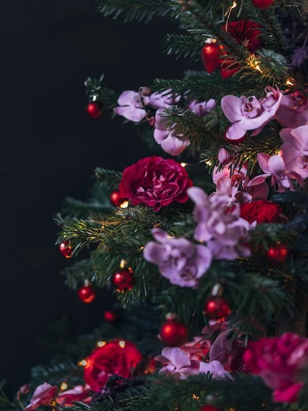 Close-up of a decorated Christmas tree with pink and red flowers, small red ornaments, and string lights.
