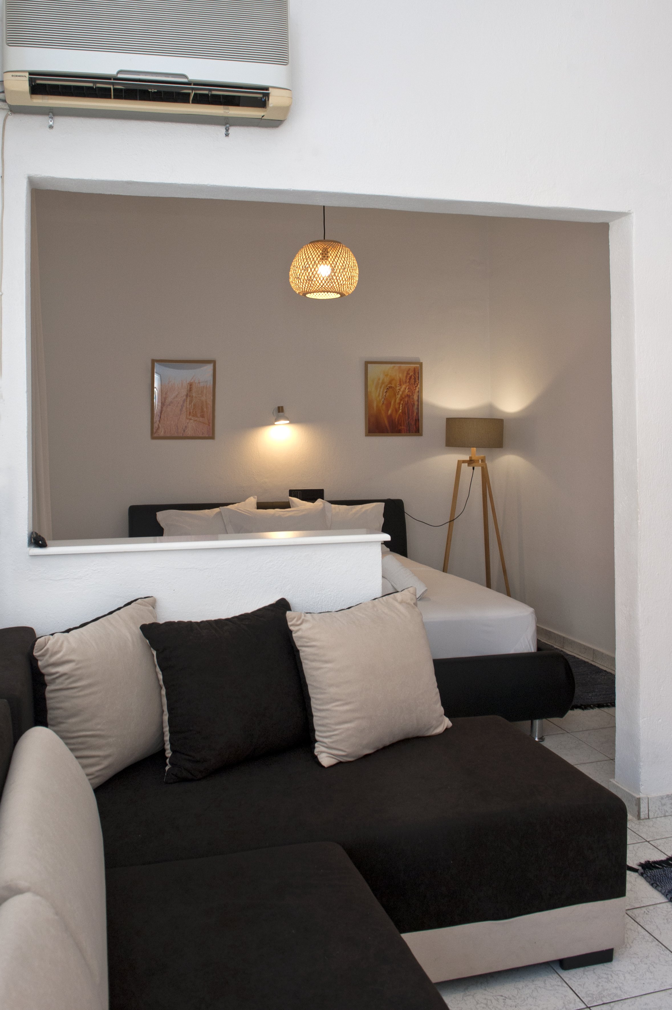 Living room with a black and a beige couch, pillows, wall art, floor lamp, and an air conditioning unit.