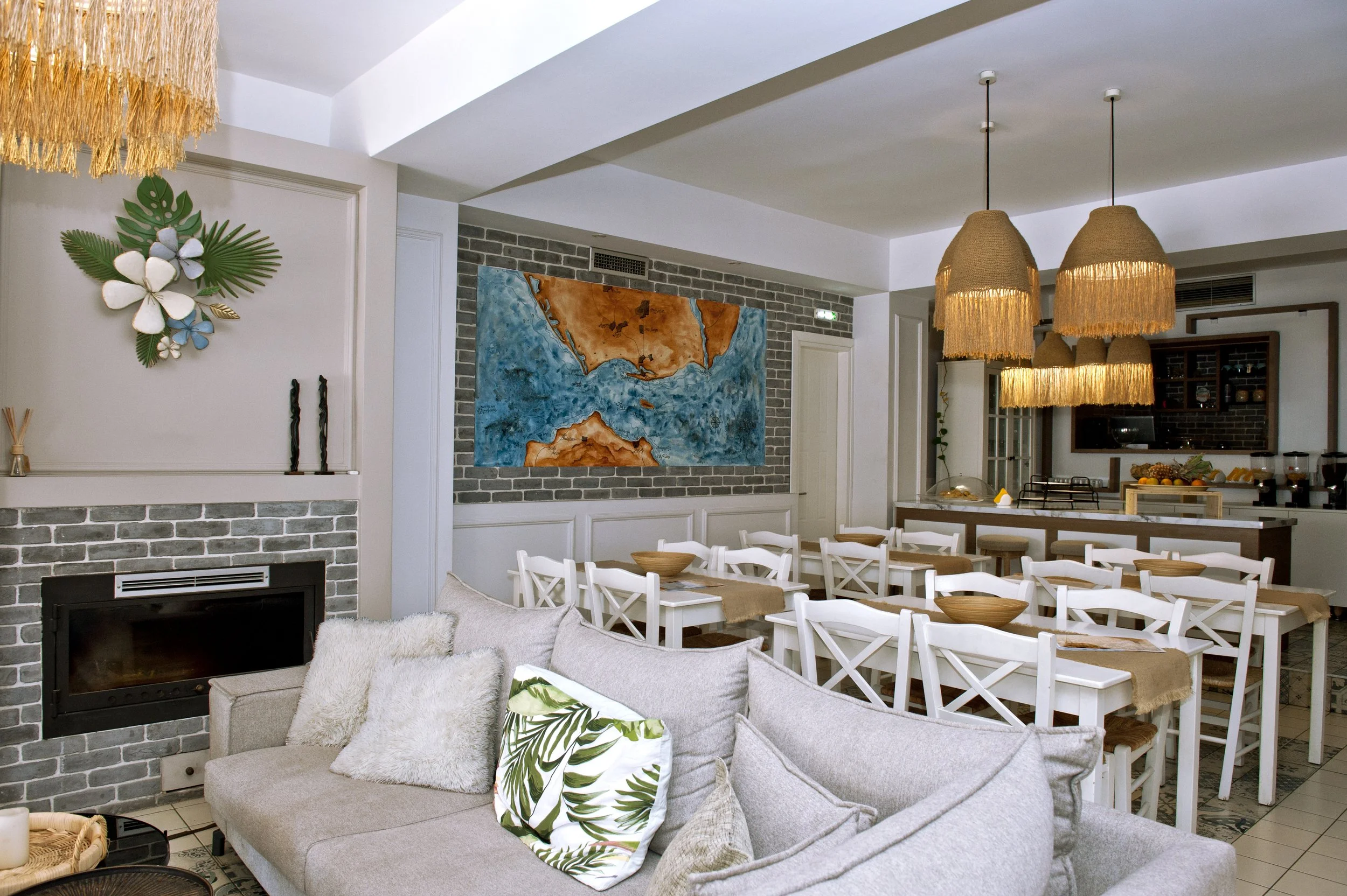 Interior view of a modern living and dining area with a gray brick fireplace, abstract wall art, hanging woven pendant lights, white dining chairs, and a beige sofa with patterned cushions.