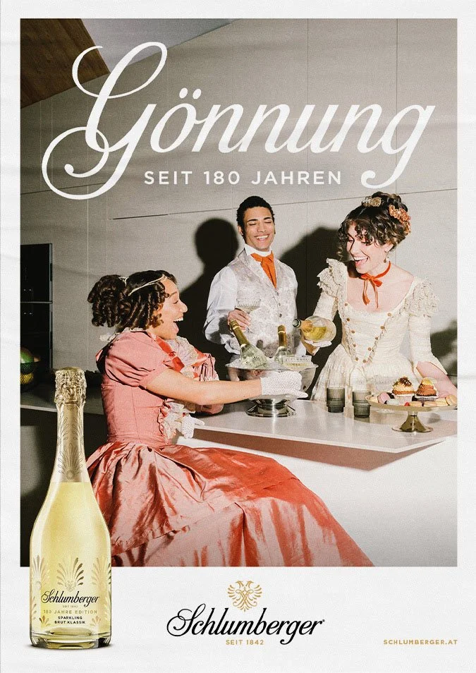 Drei Frauen in historischer Kleidung laden sich in einer gepflegten Feier an einer Bar, im Vordergrund eine Flasche Schlumberger Sekt.