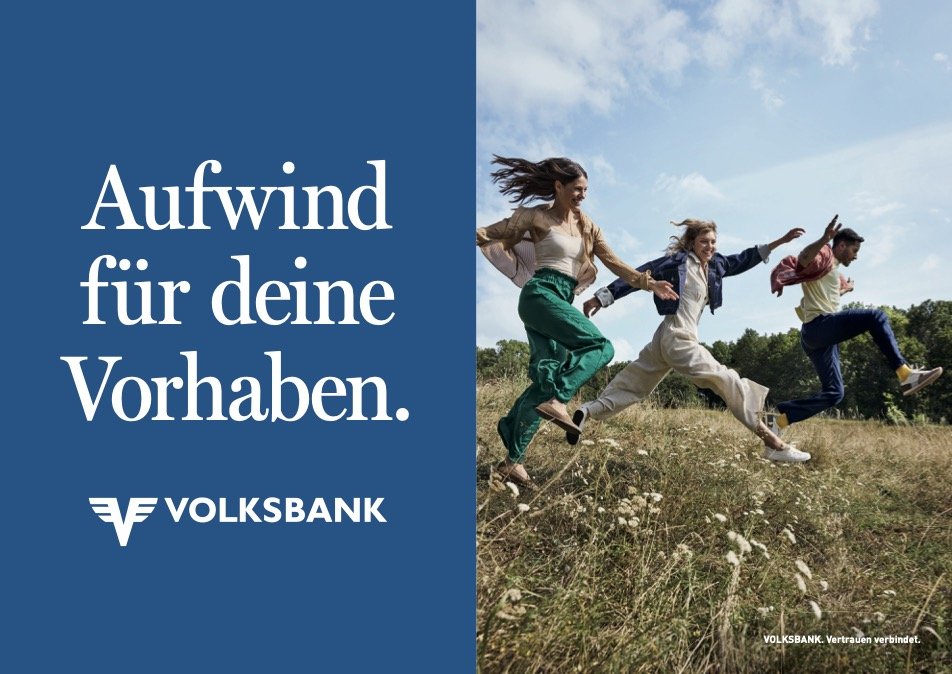 Vier Menschen springen fröhlich in einer Wiese, während sie Hand in Hand halten. Links befindet sich ein blauer Bereich mit weißen Text: 'Aufwind für deine Vorhaben.' und das Volksbank-Logo.