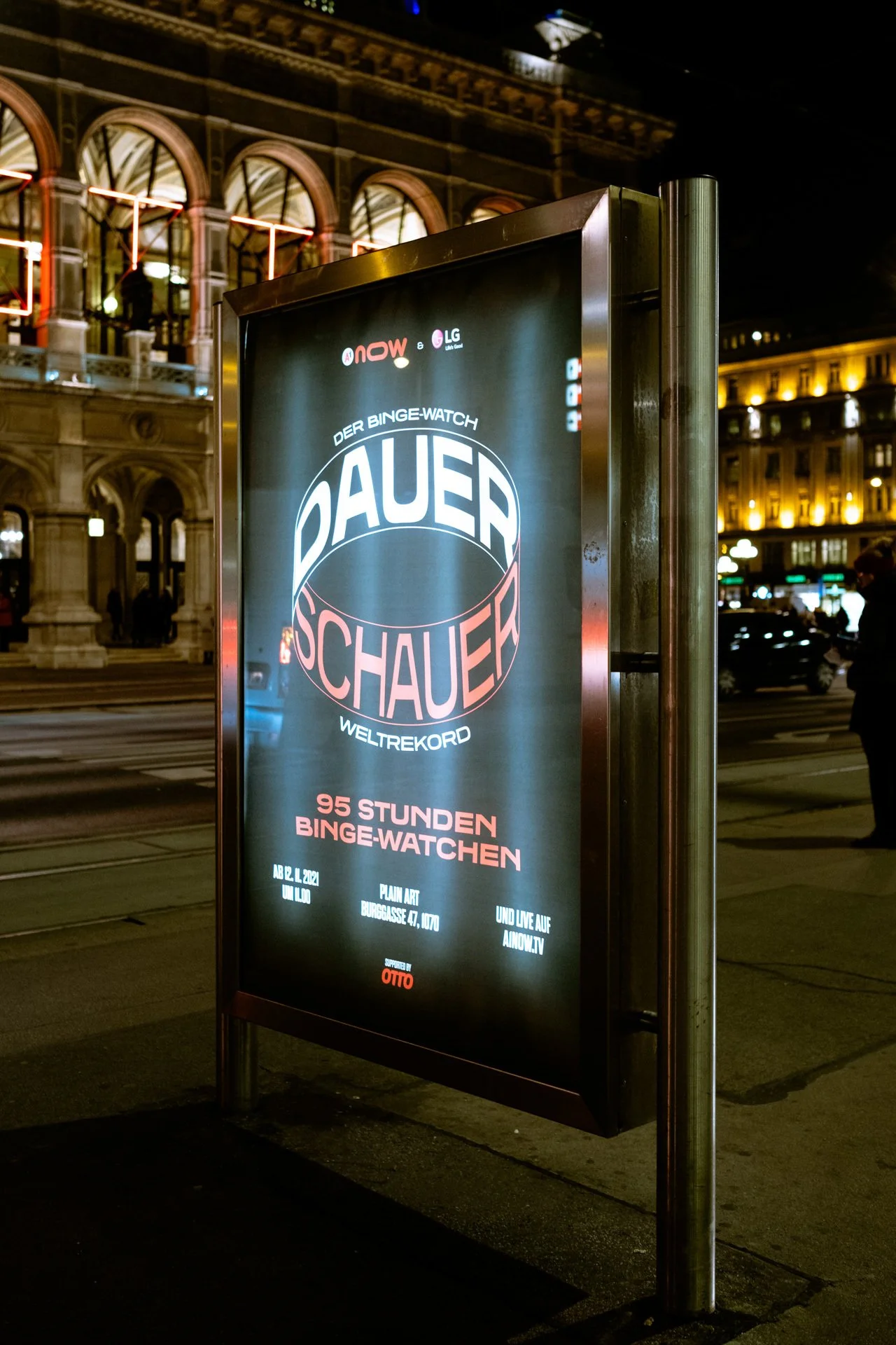Straßenwerbung für eine Binge-Watching-Event mit der Überschrift '95 Stunden Binge-Watchen', gezeigt auf einem beleuchteten Plakat in einer Stadt bei Nacht.