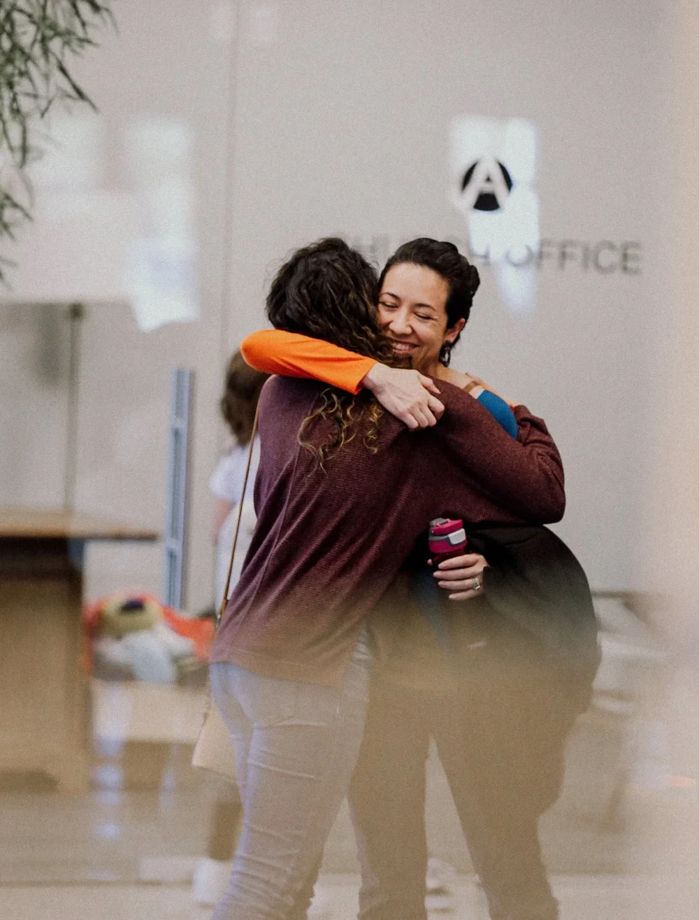 Two women hugging and smiling in an office lobby.