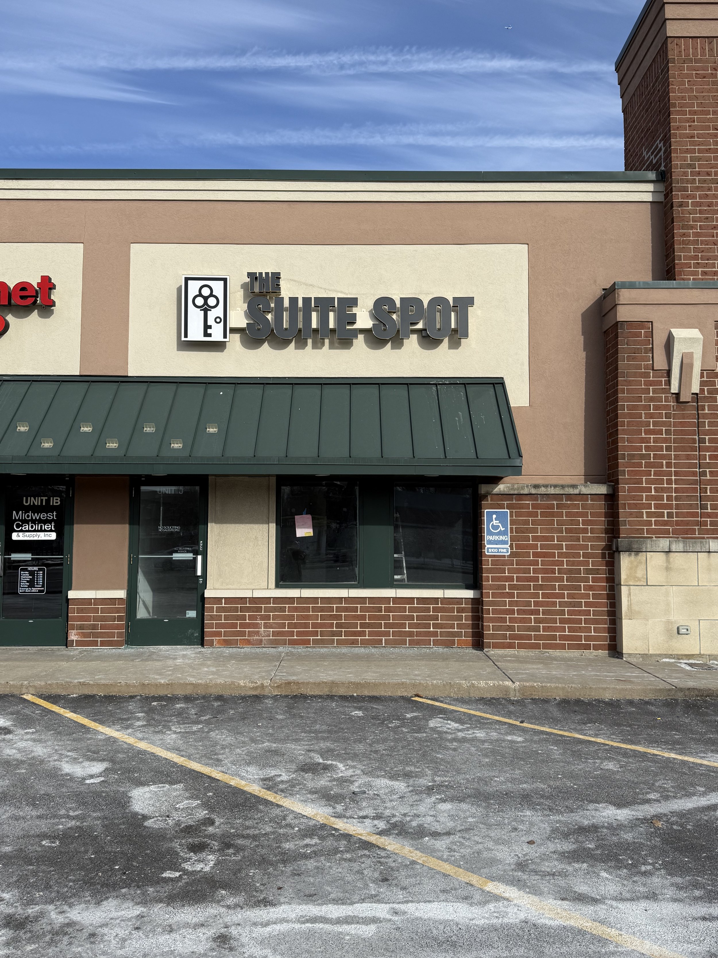 Storefront with sign 'The Suite Spot', adjacent to a unit marked 'Midwest Cabinet', showing parking area and a handicap parking sign.