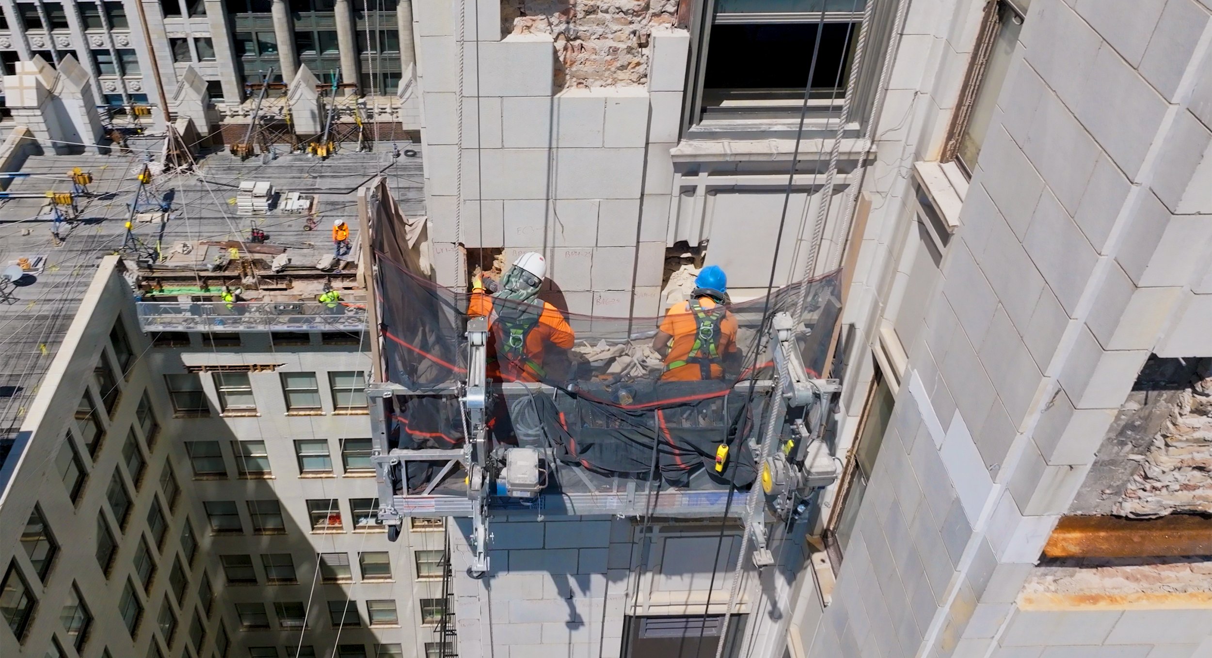 Restoration workers repairing the original terra cotta facade of the historic Pittsfield Building in Chicago from suspended swing stages.
