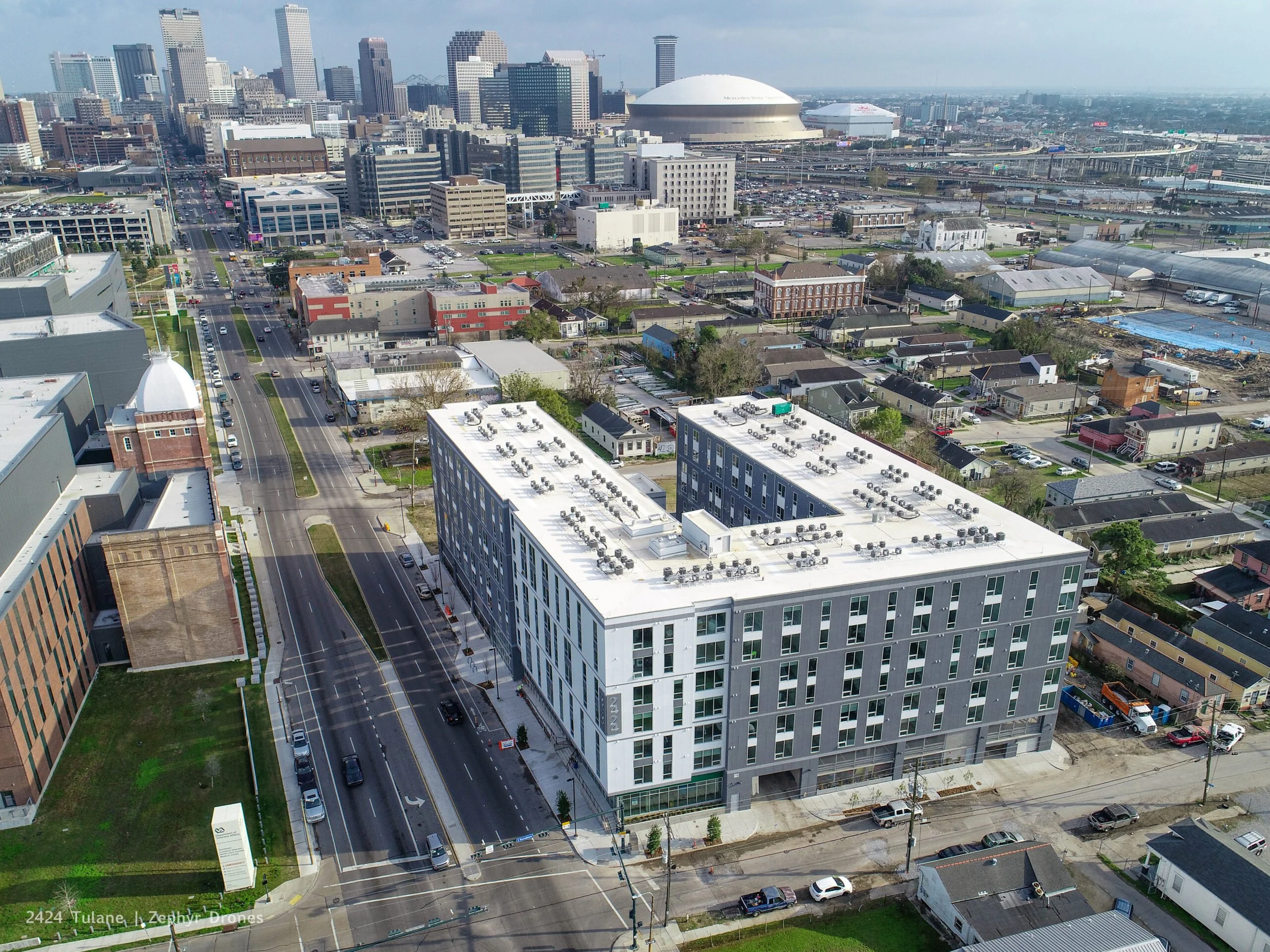 Aerial view of downtown New Orleans with a modern white building in the foreground, city skyscrapers in the background, and a mix of residential and commercial buildings.