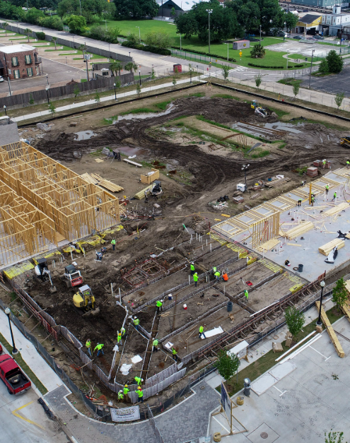 Construction site with workers and framing in progress for a new building, surrounded by dirt and construction equipment.
