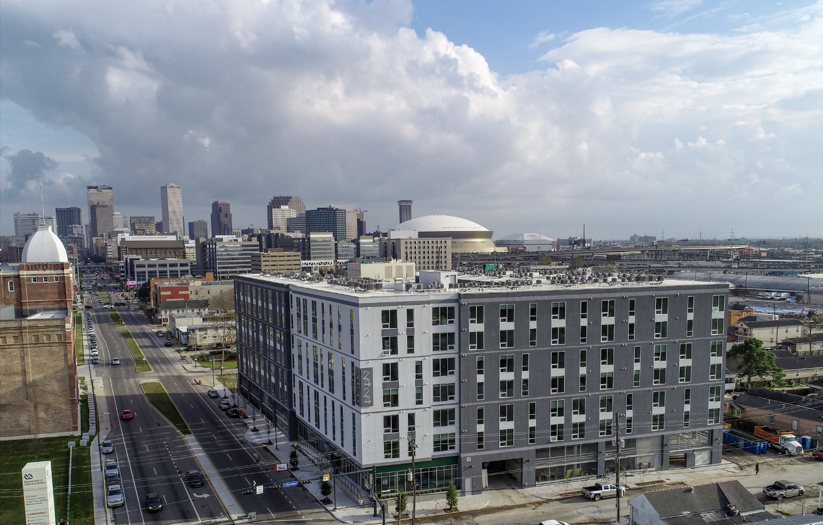 Urban cityscape with a mix of modern and historic buildings, including a large white-domed stadium, under a partly cloudy sky.