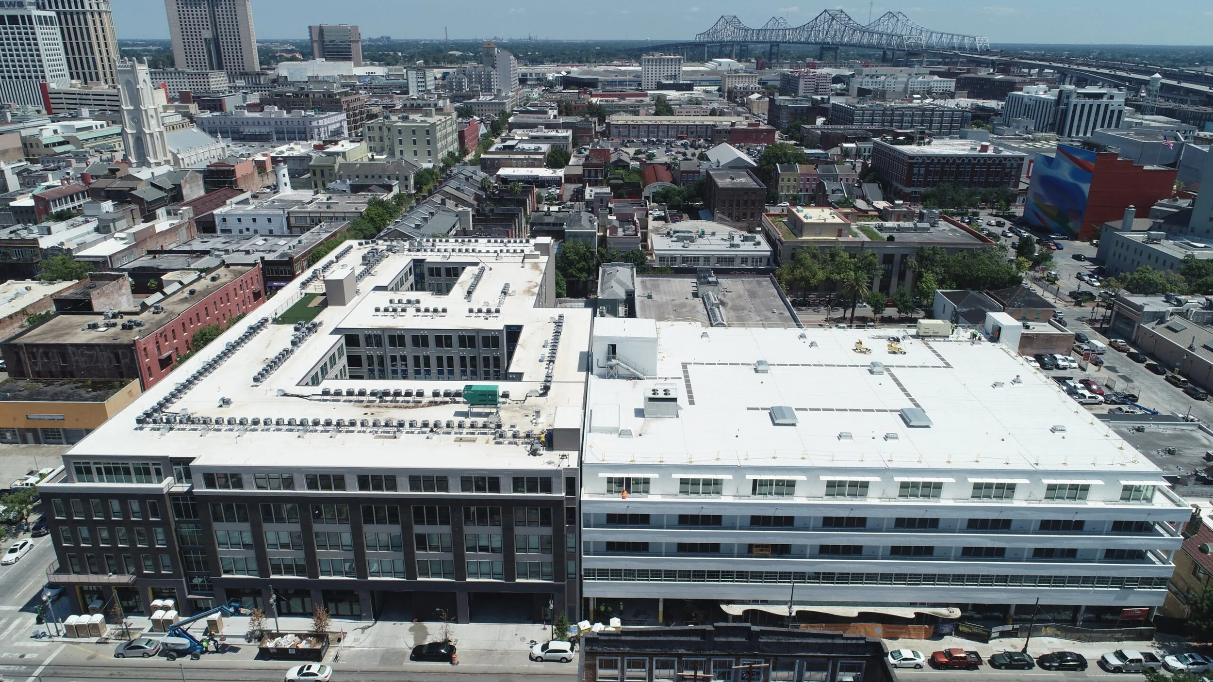 Aerial view of a city with a modern white and black building in the foreground, surrounded by various other buildings, with a bridge in the background.