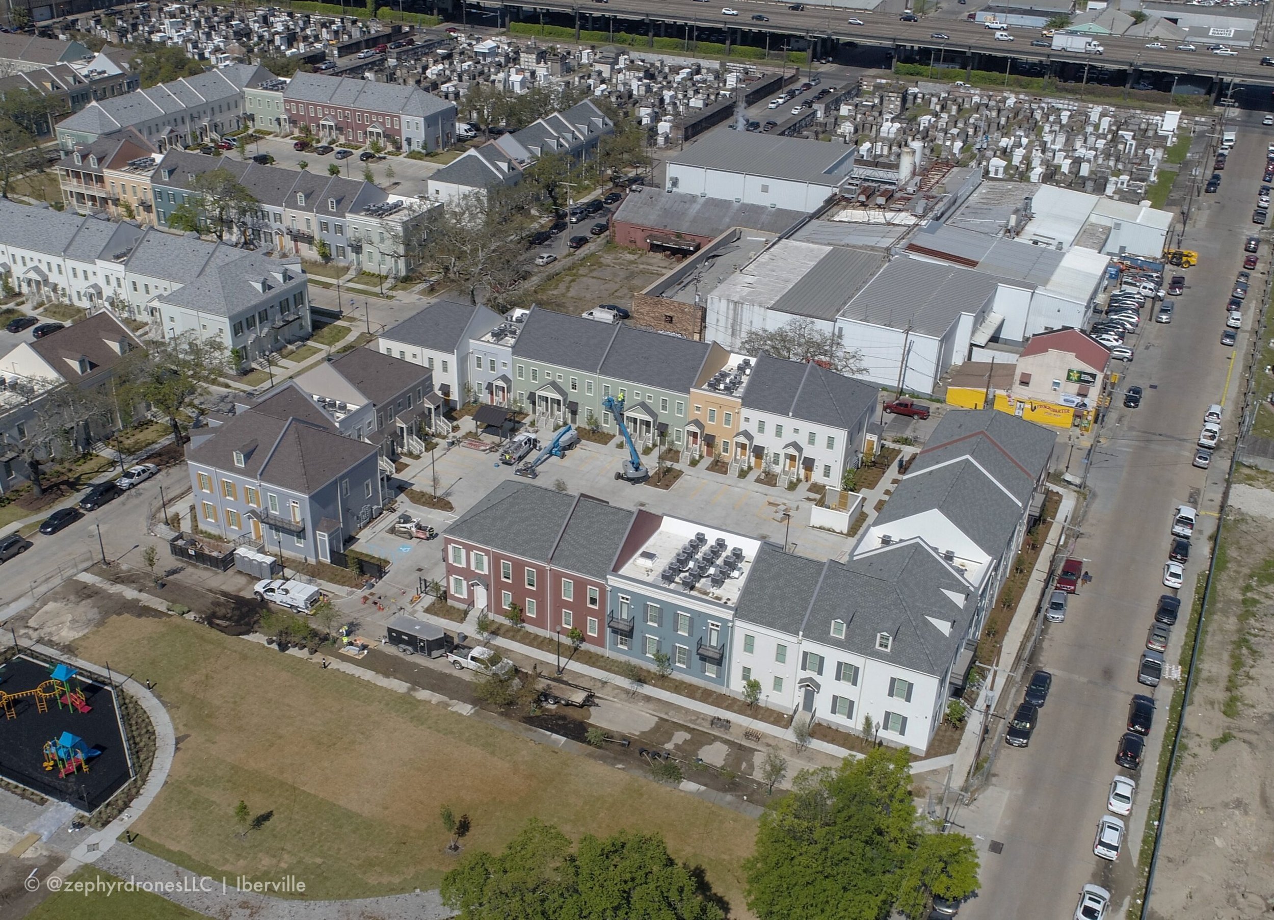 Aerial view of a residential neighborhood with colorful modern townhouses, a playground, parking lots, and industrial buildings.