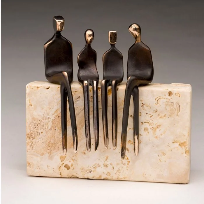 Art sculpture of four human-like figures made from metal forks, seated on a stone block.
