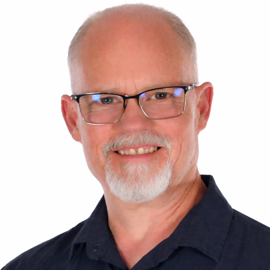 A black and white portrait of a smiling man with glasses, a beard, and short hair, wearing a collared shirt.