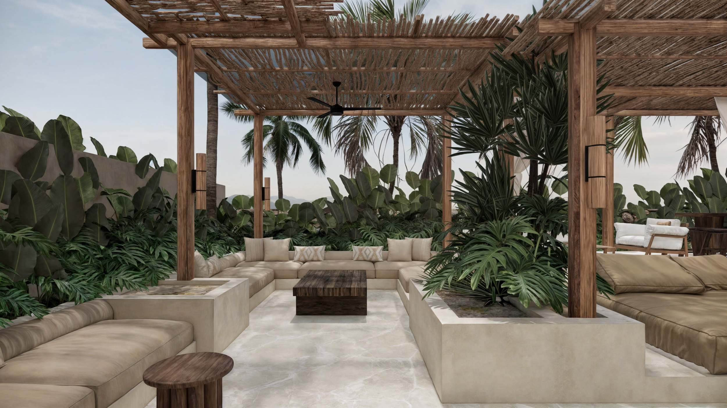 Relaxing outdoor lounge area with cream-colored sectional sofas, wooden coffee table, lush tropical plants, and a thatched wooden roof with ceiling fans, overlooking a beach with palm trees.