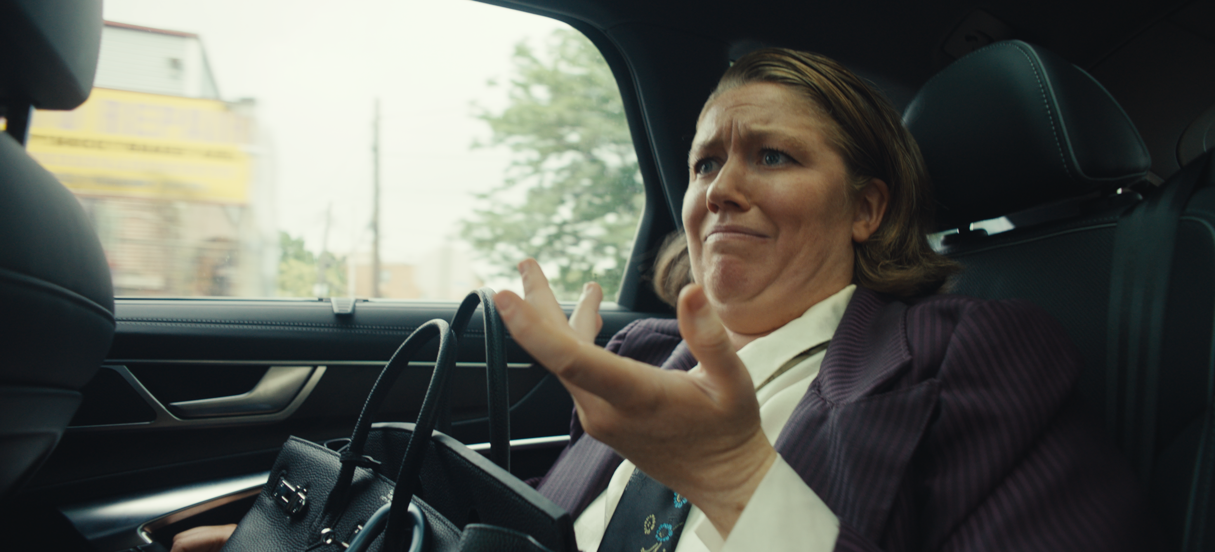 A woman with a distressed expression gesturing with her hands inside a car.