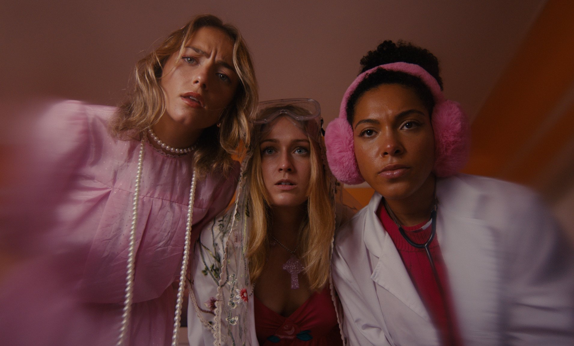 Three women dressed as medical professionals and a patient, looking at a camera, with surprised or confused expressions in a close-up shot.