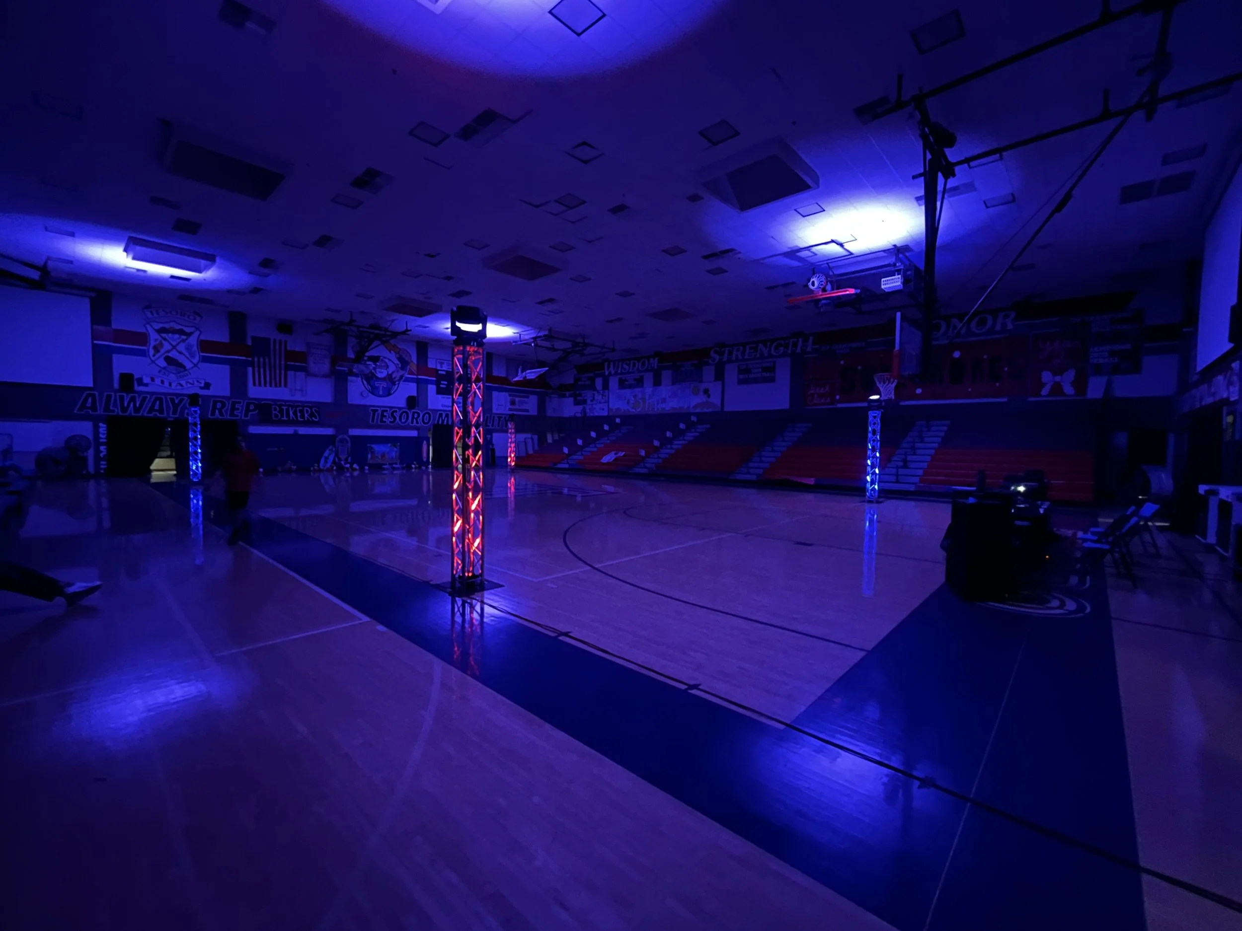 Dimly lit gymnasium with purple and blue lighting, basketball hoops, and padded walls with motivational words in the background.
