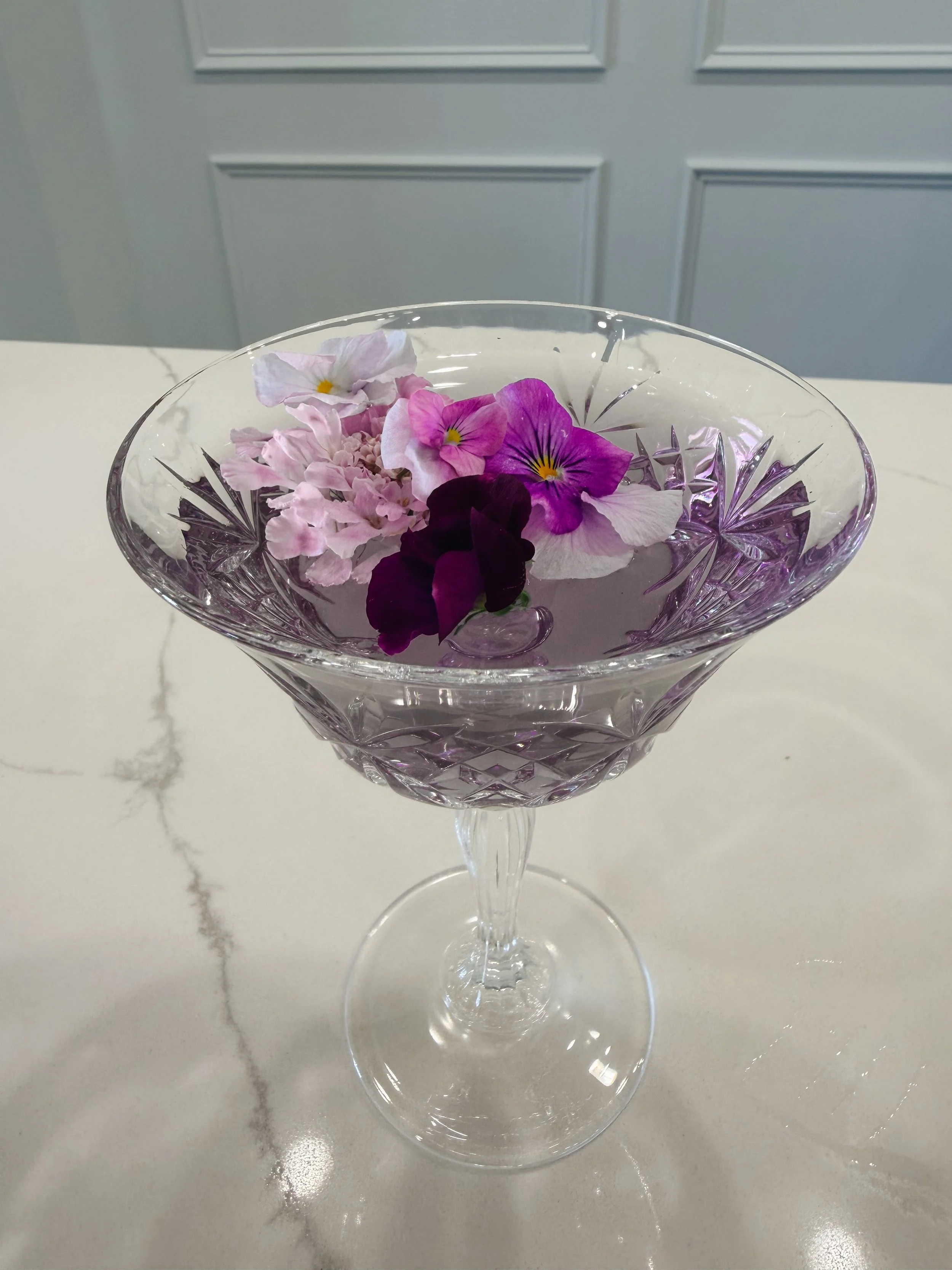 A crystal glass bowl with pink and purple flowers floating on water, placed on a white surface.