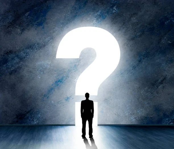 Person standing in front of a large illuminated question mark with a dark, textured background.