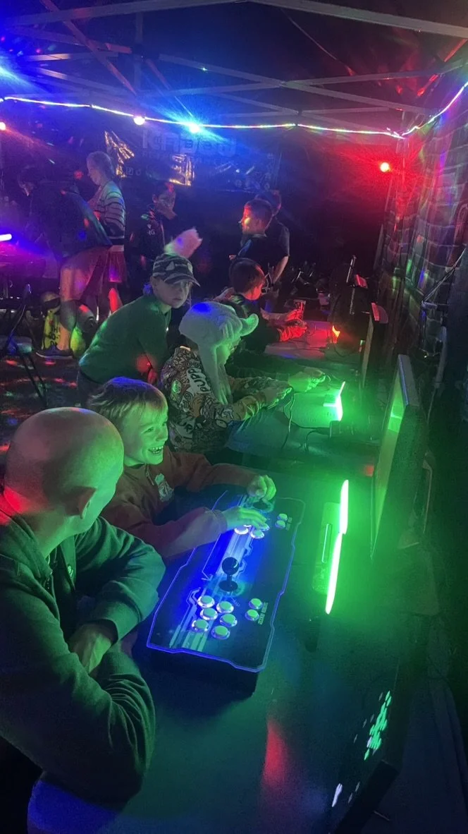 Teenagers playing arcade fighting game in a neon-lit arcade.