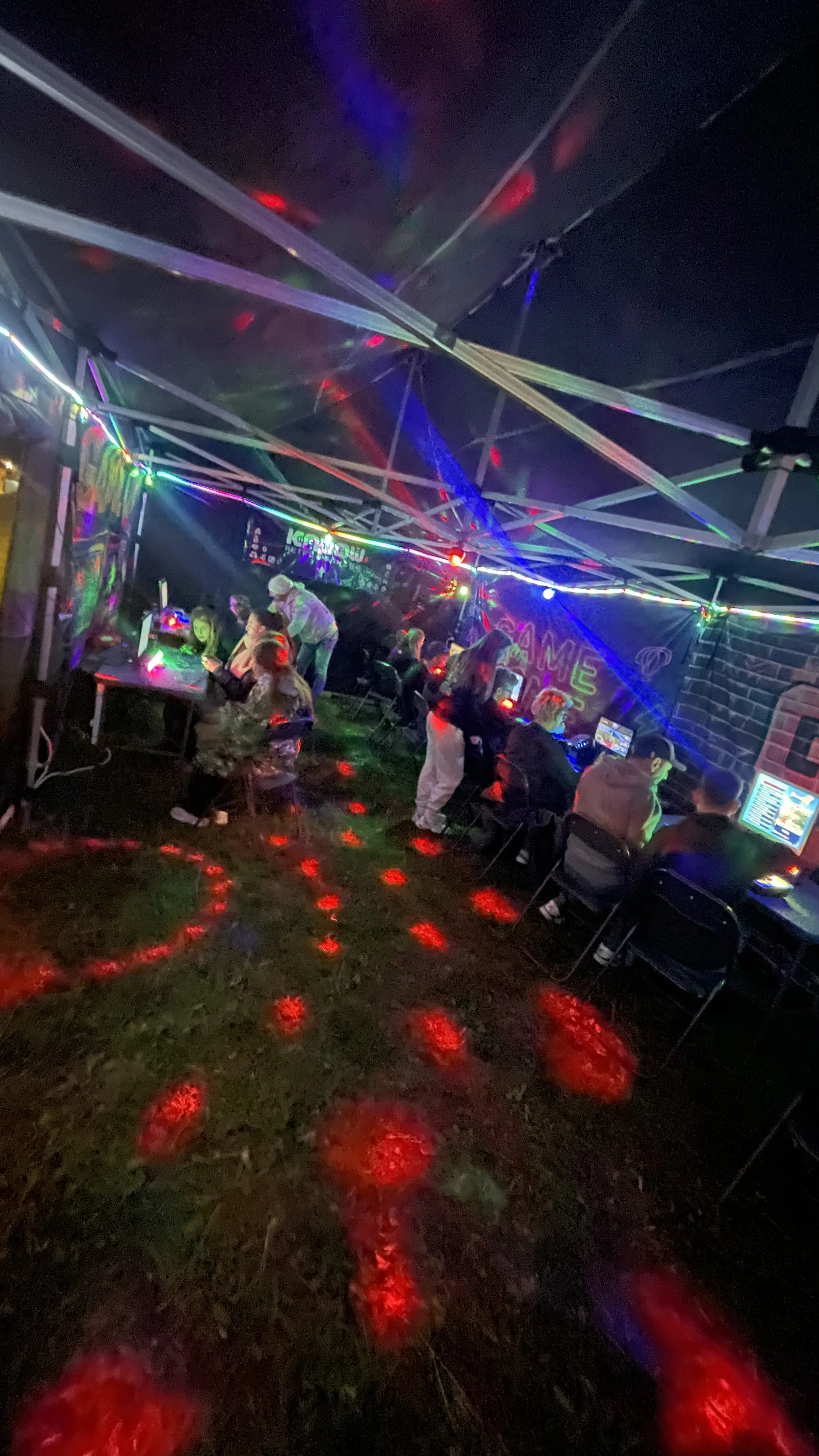 Indoor gaming arcade with children and teenagers playing video games under colorful neon lights and disco effects