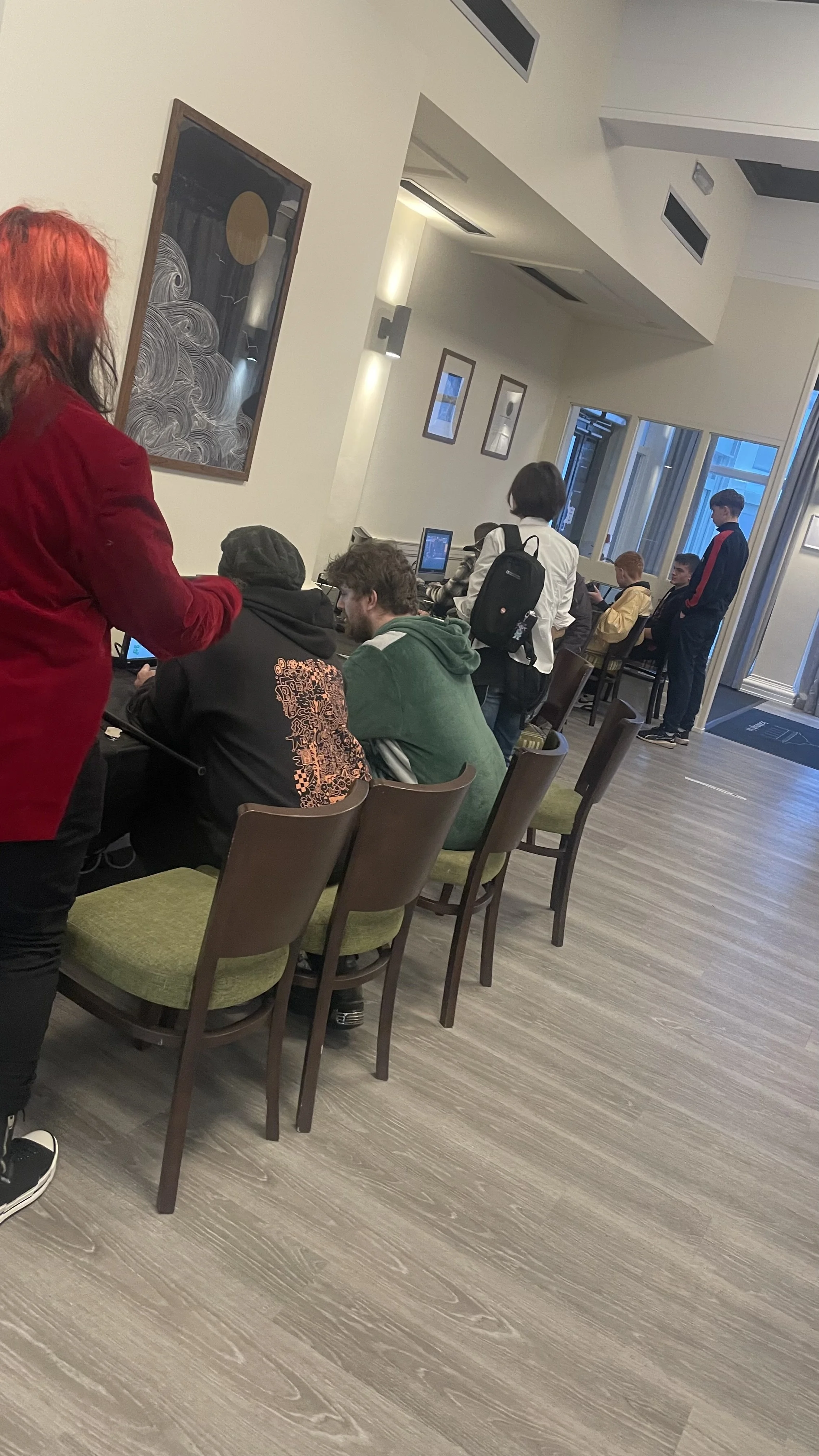People sitting and standing around a table near a window in a modern cafe or restaurant.