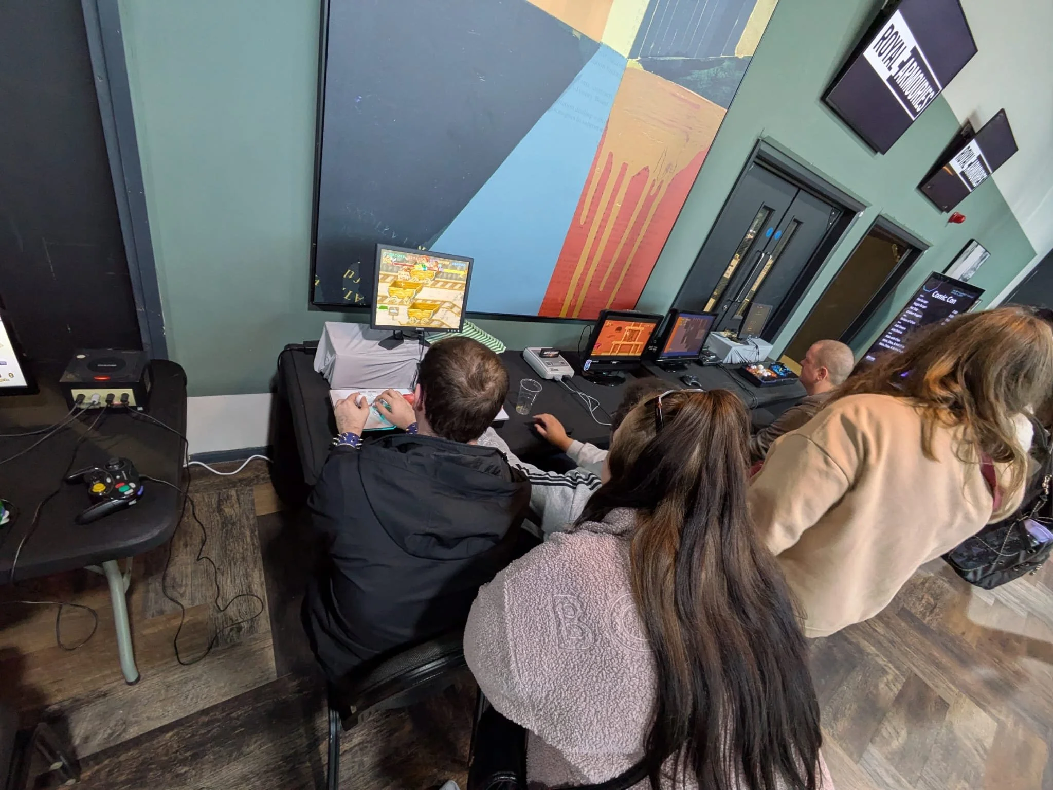 People playing and watching video games on computers and consoles in a gaming room or arcade.