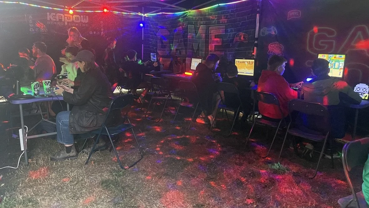 People playing video games at an arcade or gaming event with colorful lights and gaming monitors.