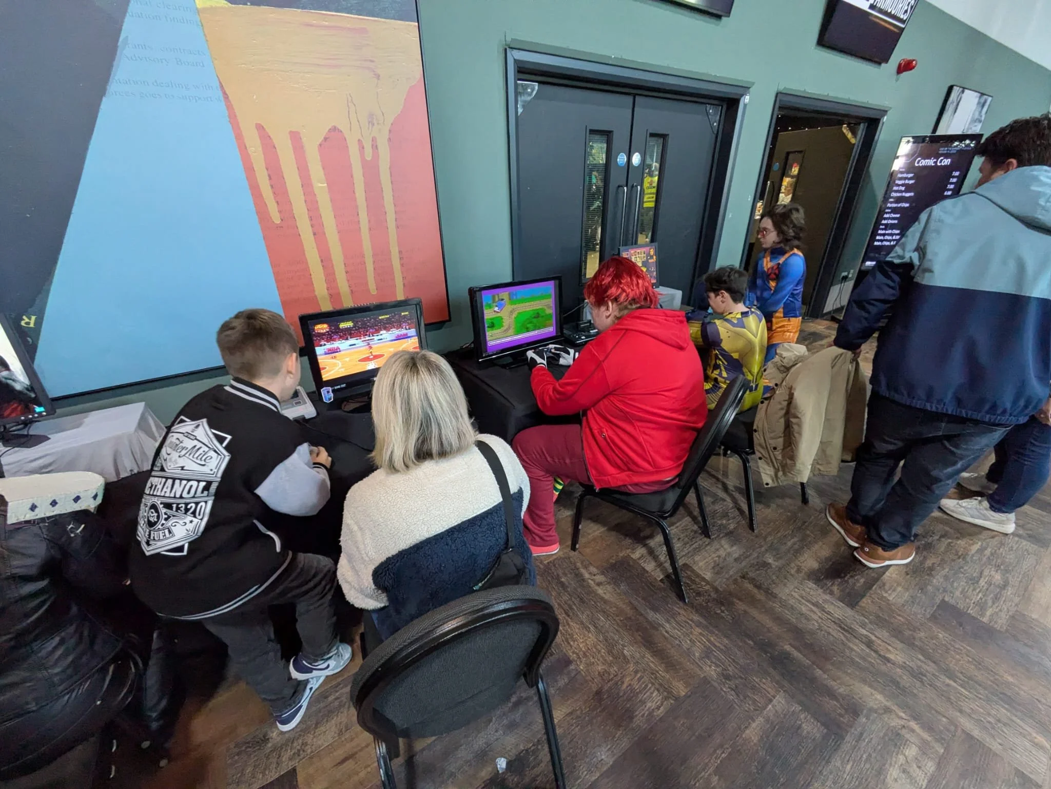 Group of people, including children and adults, playing arcade games at a gaming event.