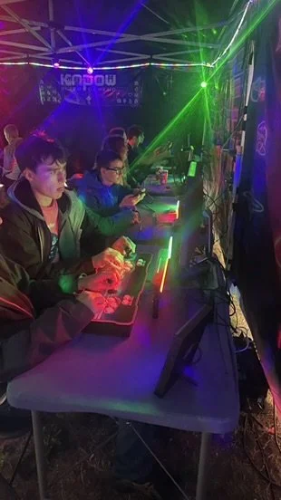 Group of young people playing video games at an arcade with colorful laser lights and glowing game controllers.