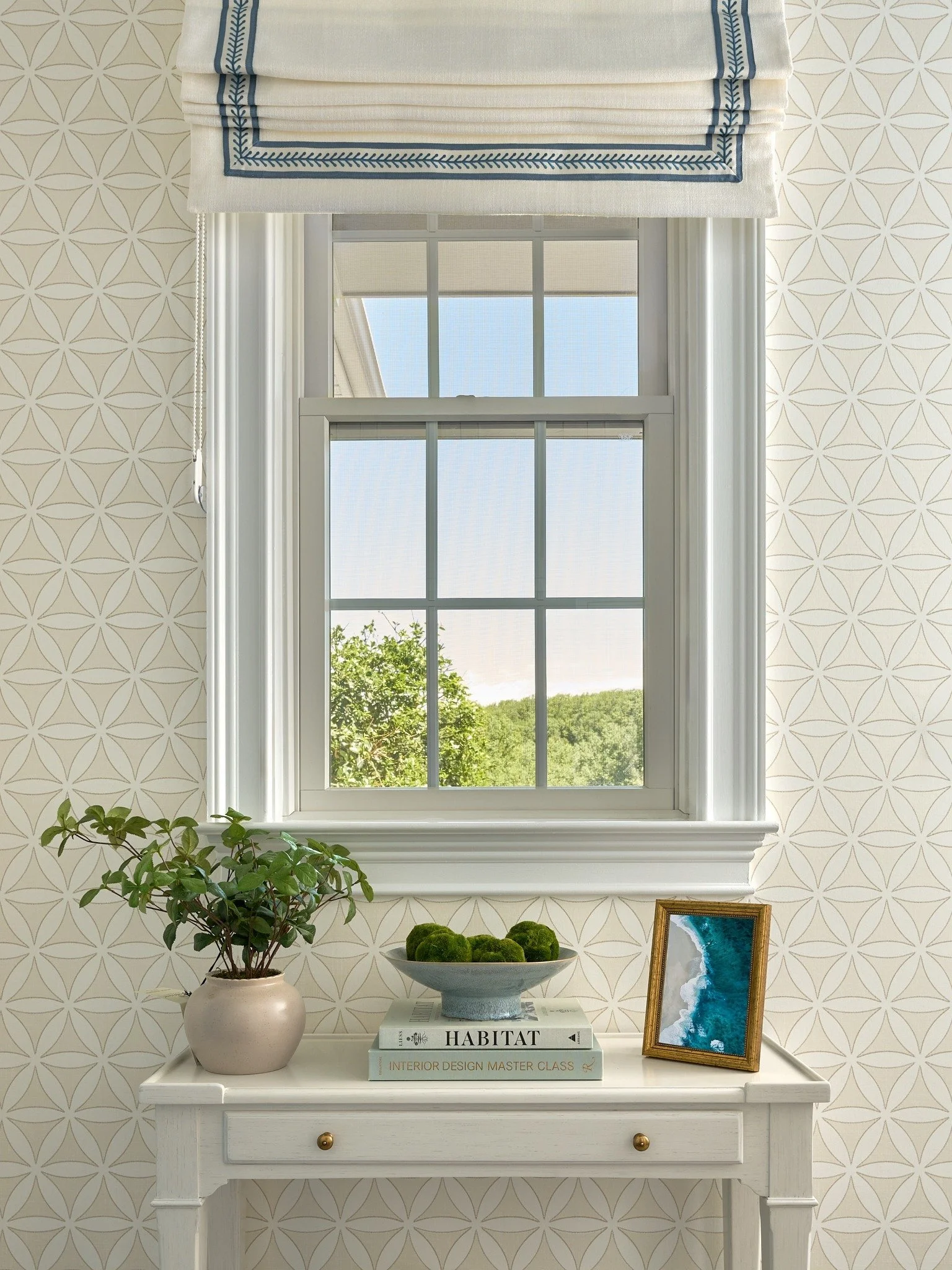 Custom Roman shade with blue embroidered trim above a styled console table in a patterned Maryland entryway.