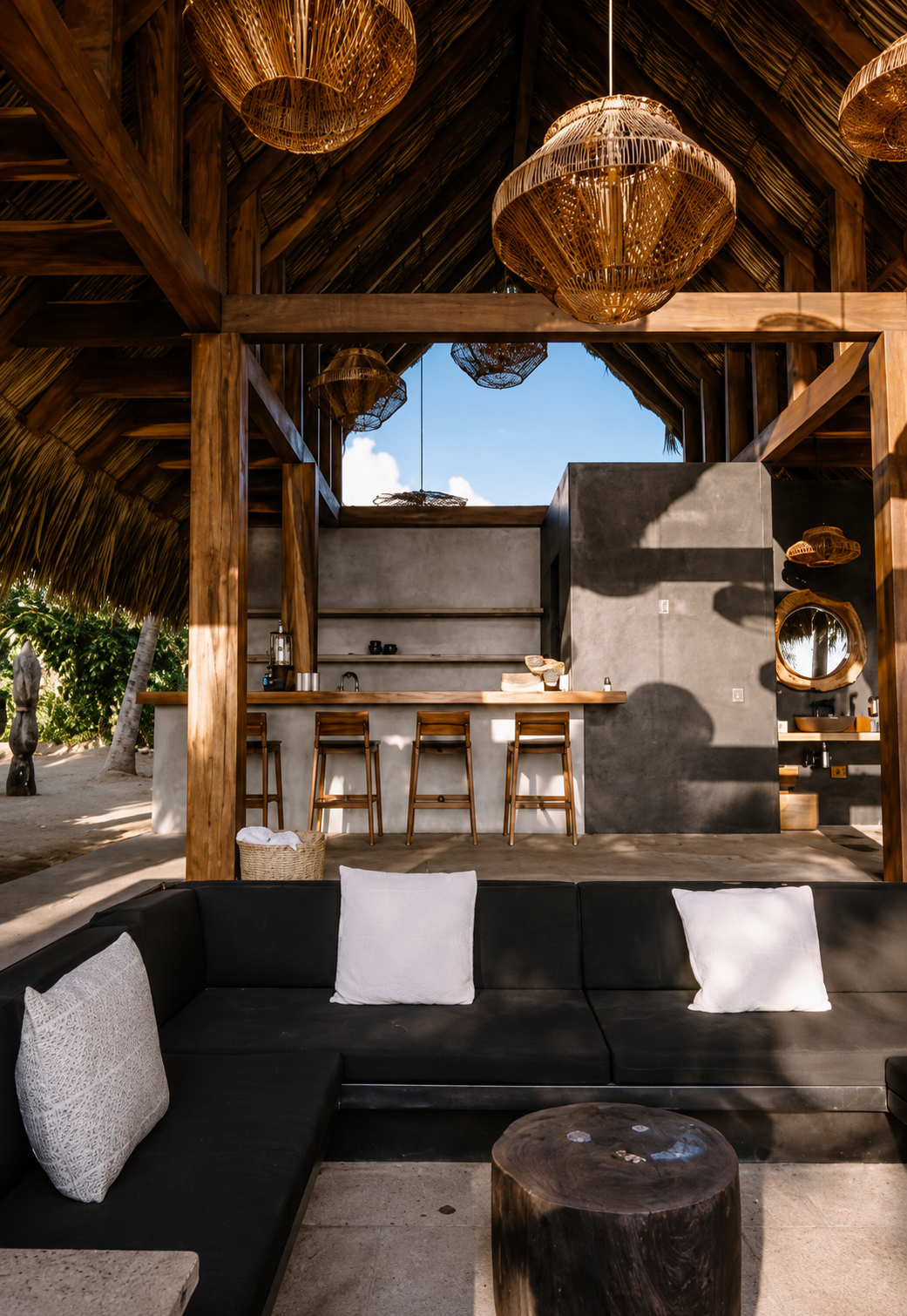 Open-air tropical pavilion with thatched roof, wood beams, outdoor kitchen bar, woven pendant lights, and modern lounge seating.