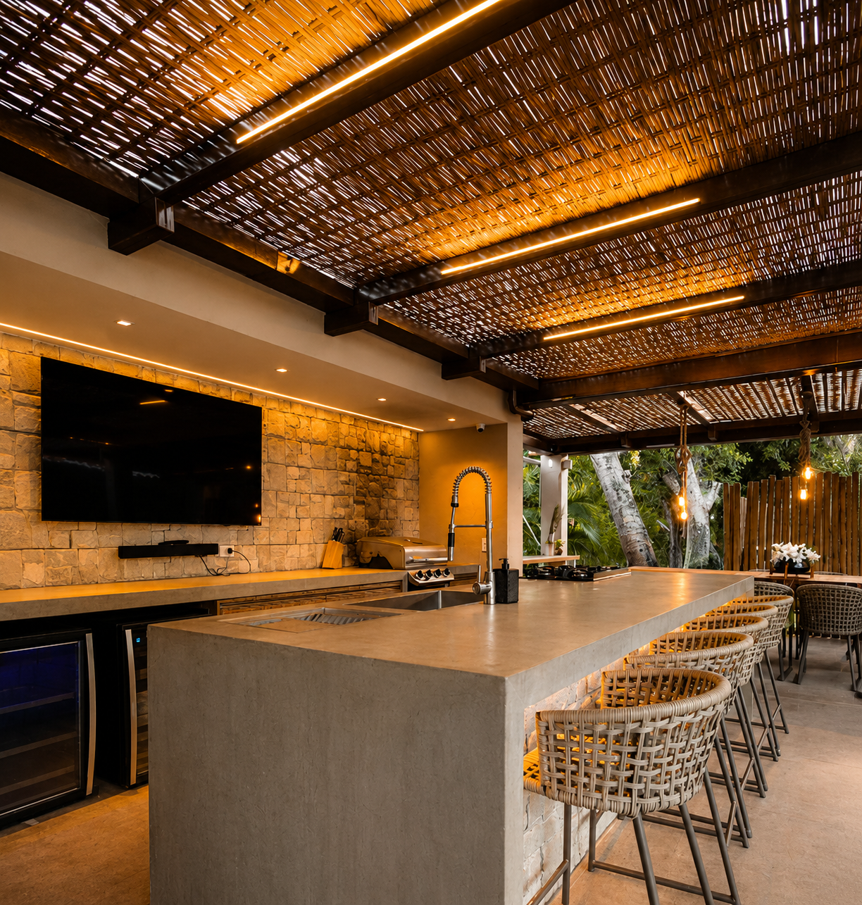 Luxury outdoor kitchen with concrete island, woven bar stools, stone accent wall, built-in grill, and illuminated pergola ceiling.