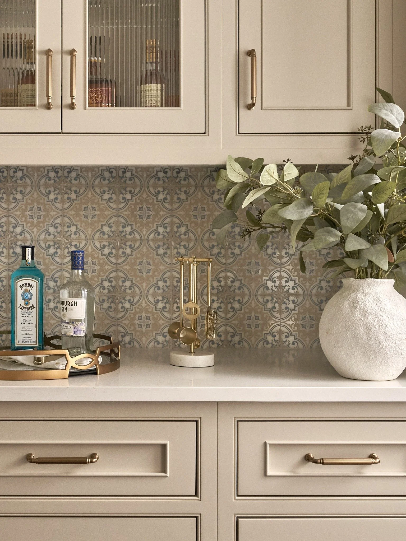 Close-up of a Maryland butler’s pantry with patterned blue and taupe tile, brass hardware, reeded glass cabinets, and a styled bar counter.
