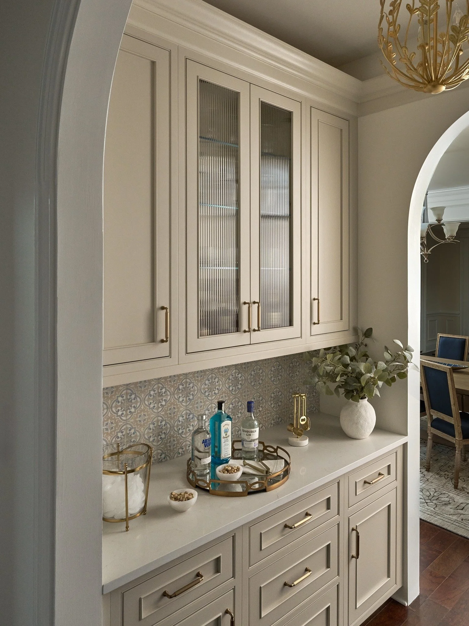 Custom Maryland home bar with reeded glass cabinets, a blue and taupe tile backsplash, brass accents, and an arched opening.